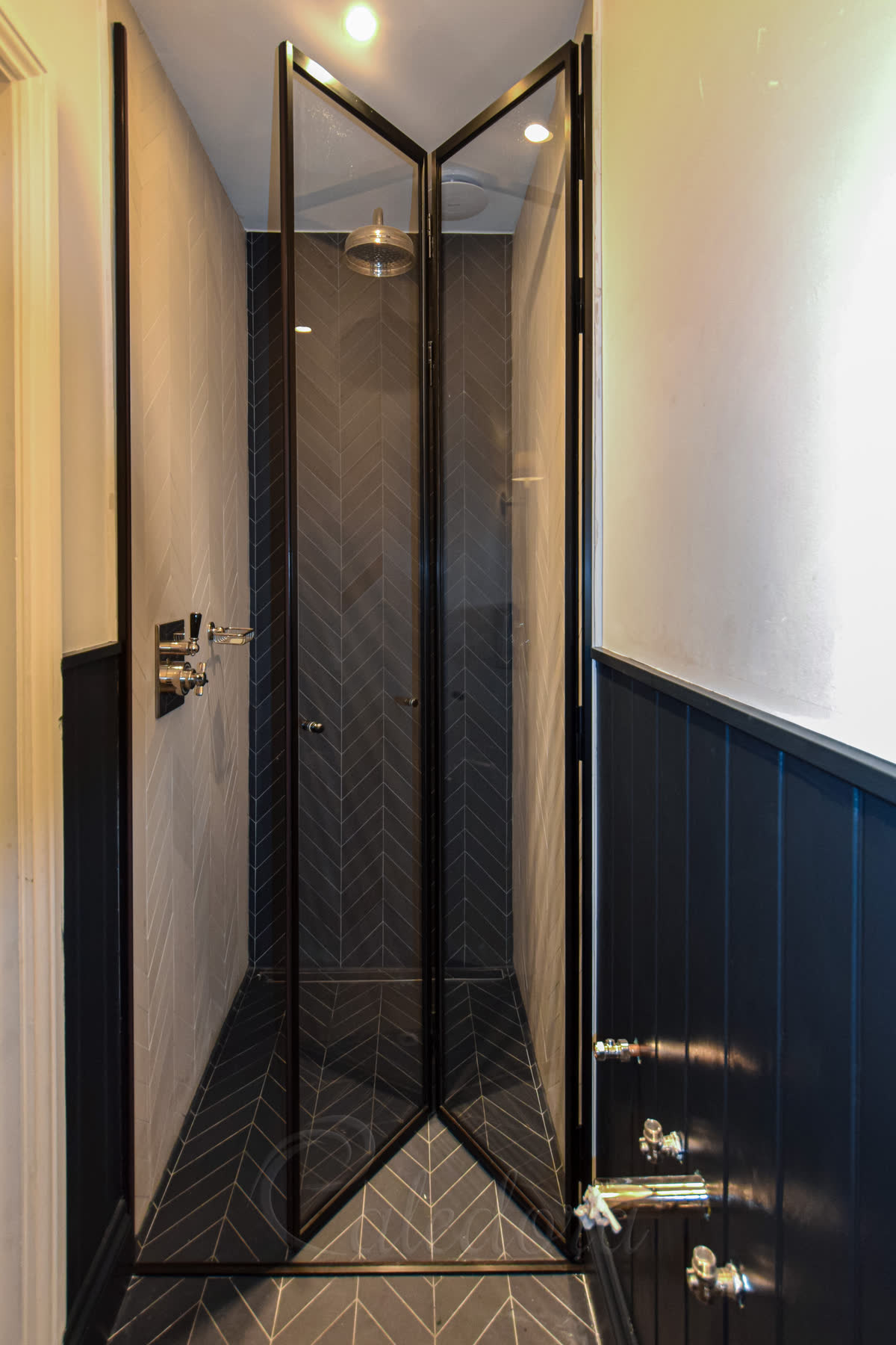 Black framed bifold shower door in a luxury bathroom with herringbone tiles