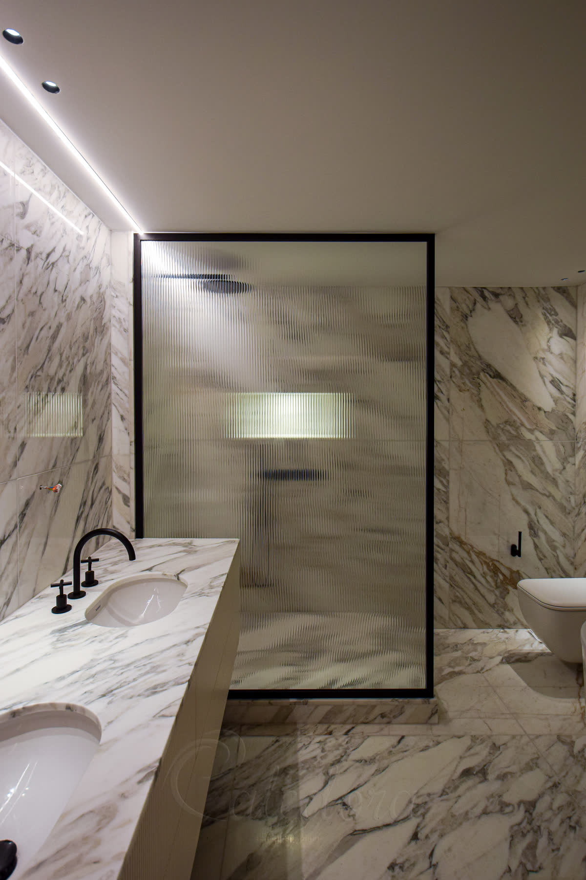 Black framed full-height shower screen with reeded glass in a marble bathroom