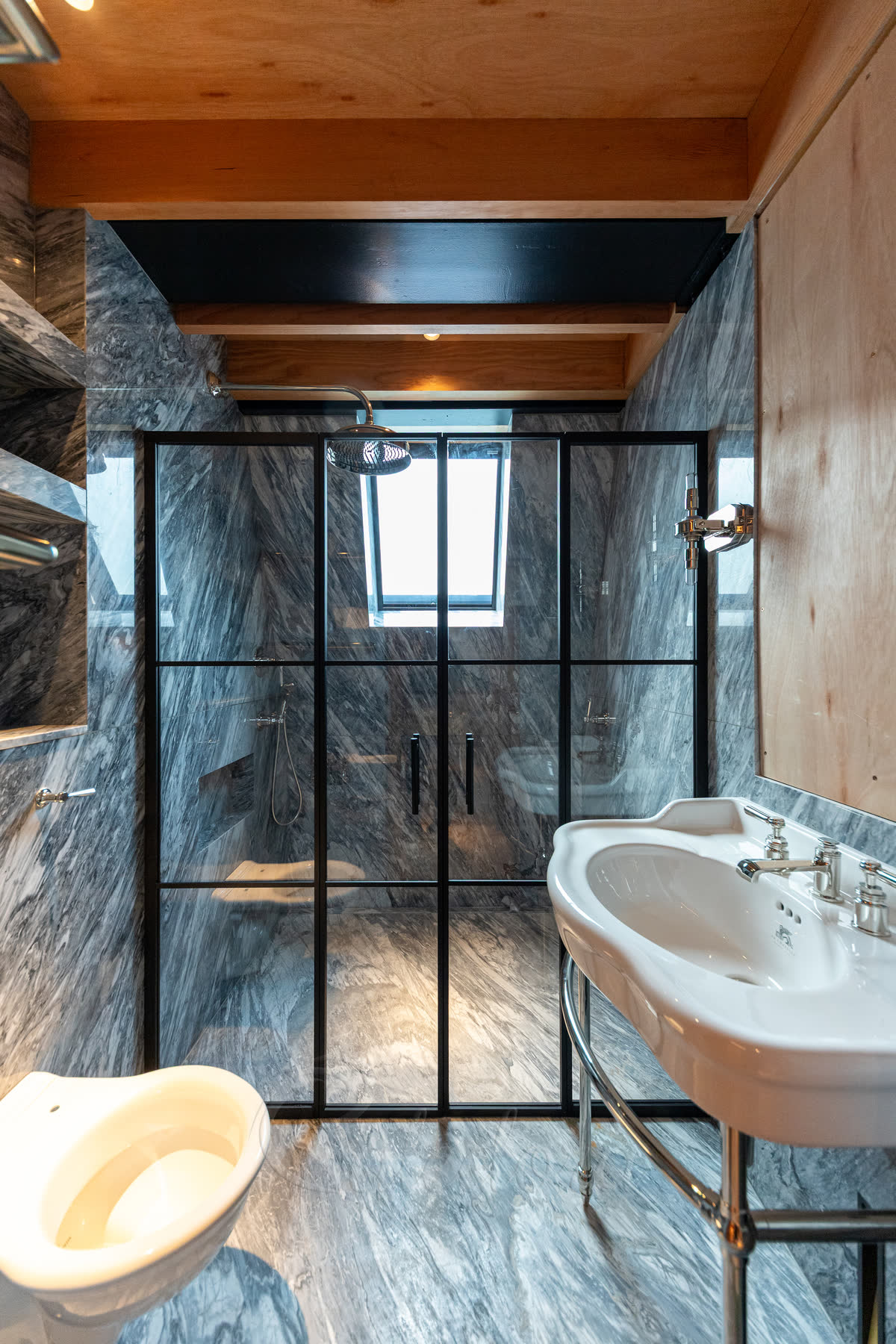 Black grid shower enclosure with double swing doors in a marble bathroom