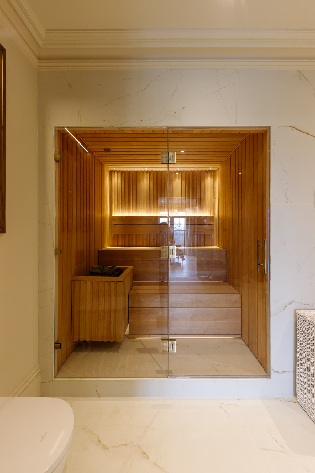 Antique brass hinges and bar handle on a glass sauna door — cedar-lined sauna interior with bench seating, set in a marble-clad alcove