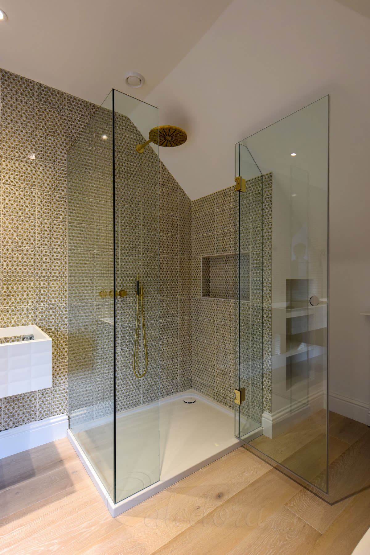 Brass shower enclosure in a loft bathroom — brass profiles following the sloped roof line with clear glass panels