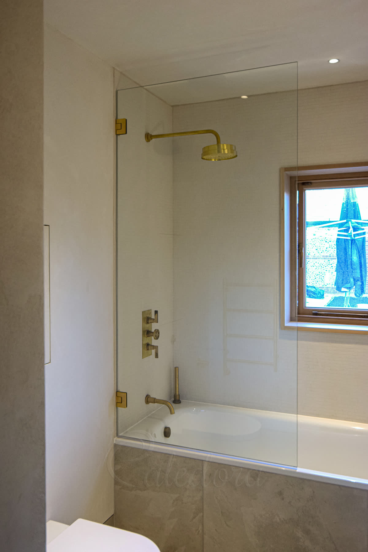 Brushed brass bath shower screen with brushed brass frame over a freestanding bath