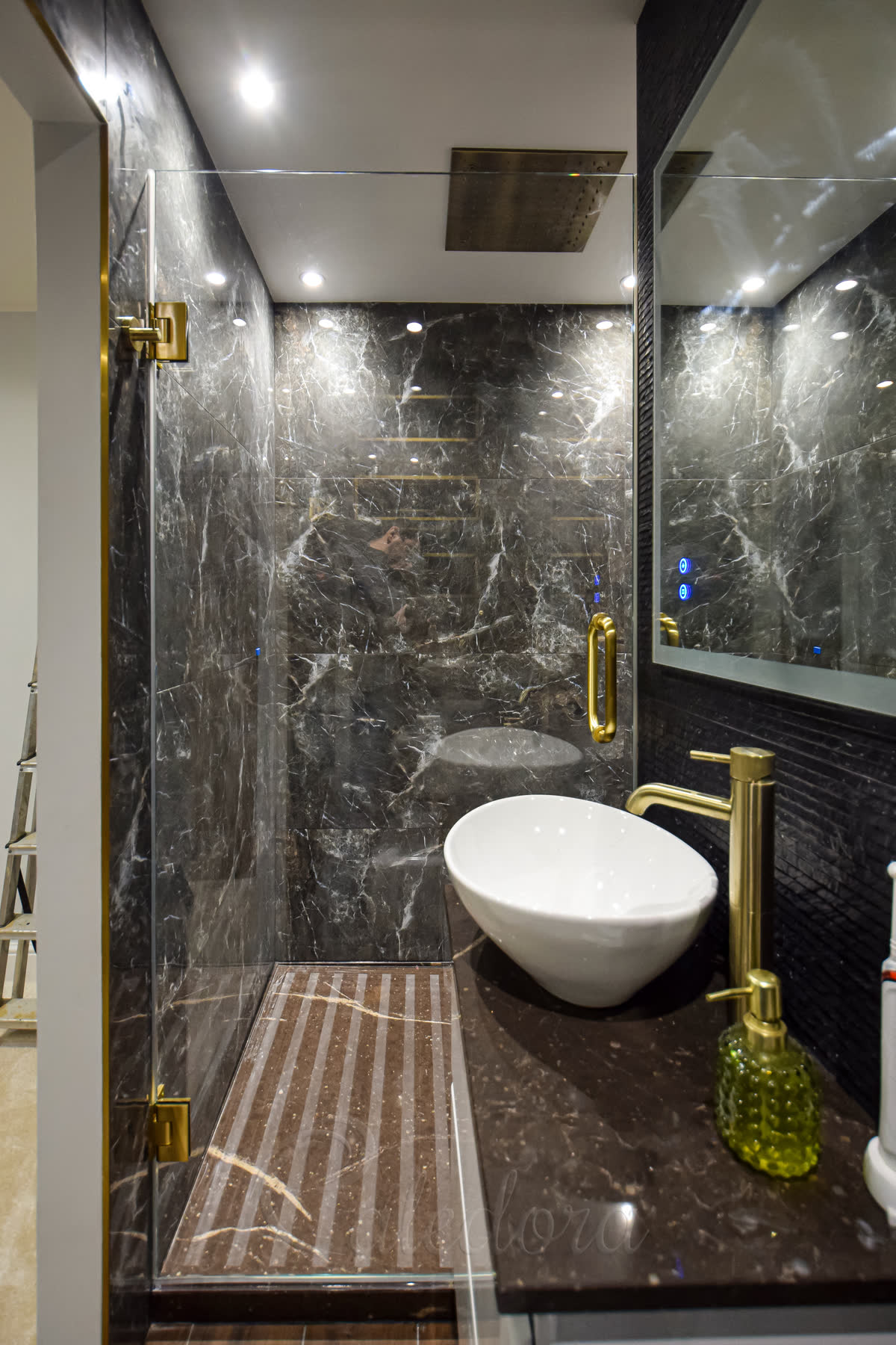 Brushed brass frameless shower door with brushed brass hinges and handle against dark marble walls