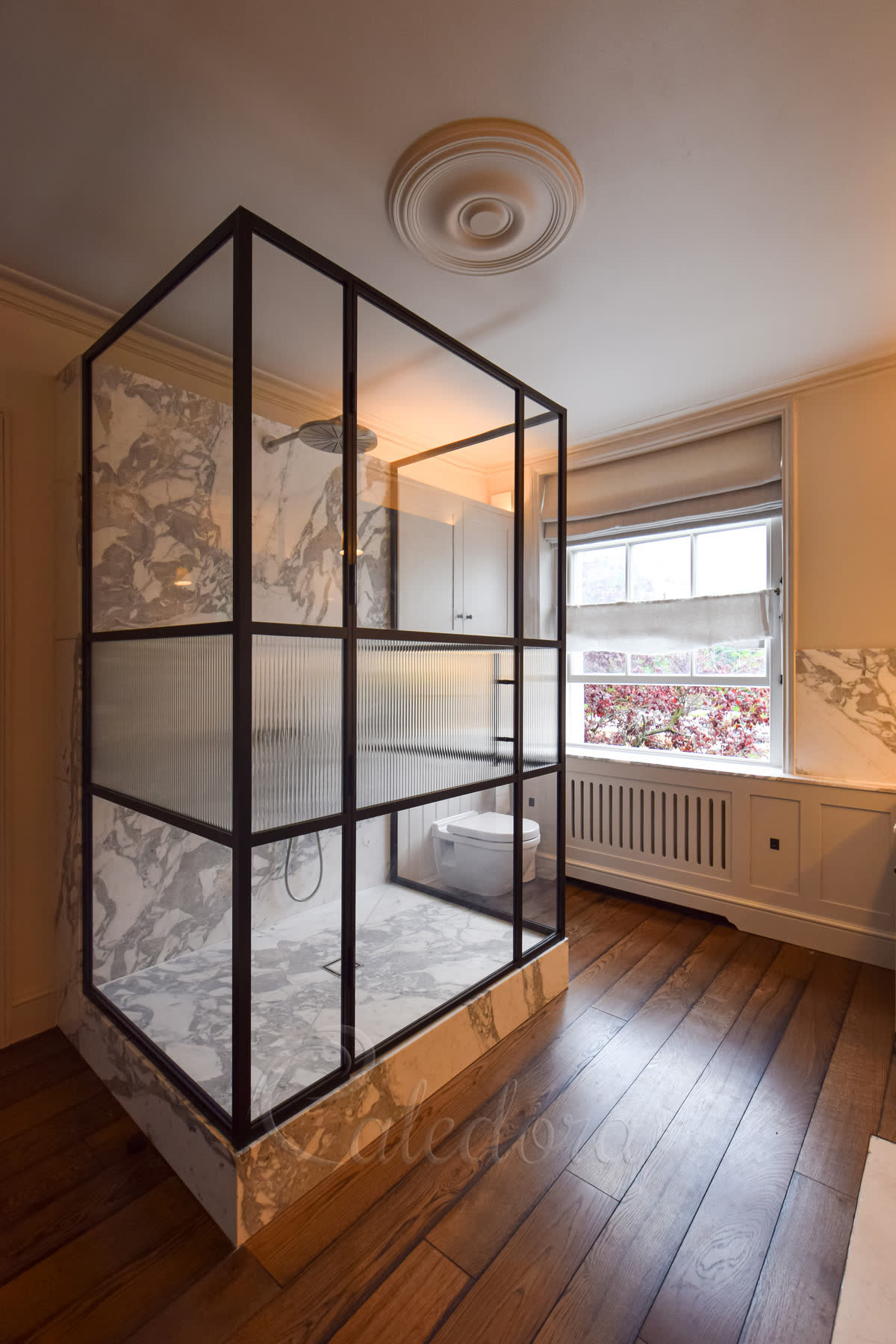 Clear and reeded glass in the same panel — a three-sided shower enclosure in a satin black grid frame, ultra-clear laminated glass top and bottom with a reeded band laminated across the middle of each side, standing on a marble tray in a period bathroom with an oak floor