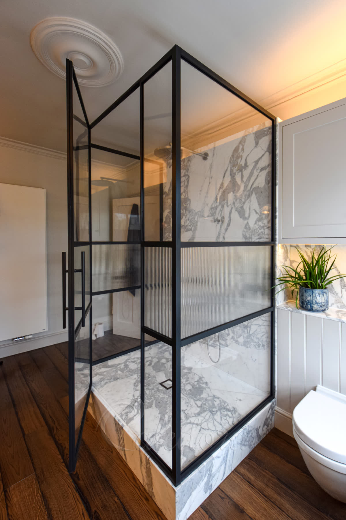Three-sided shower enclosure combining clear glass top and bottom with a reeded band across the middle of each black grid panel, on a marble tray