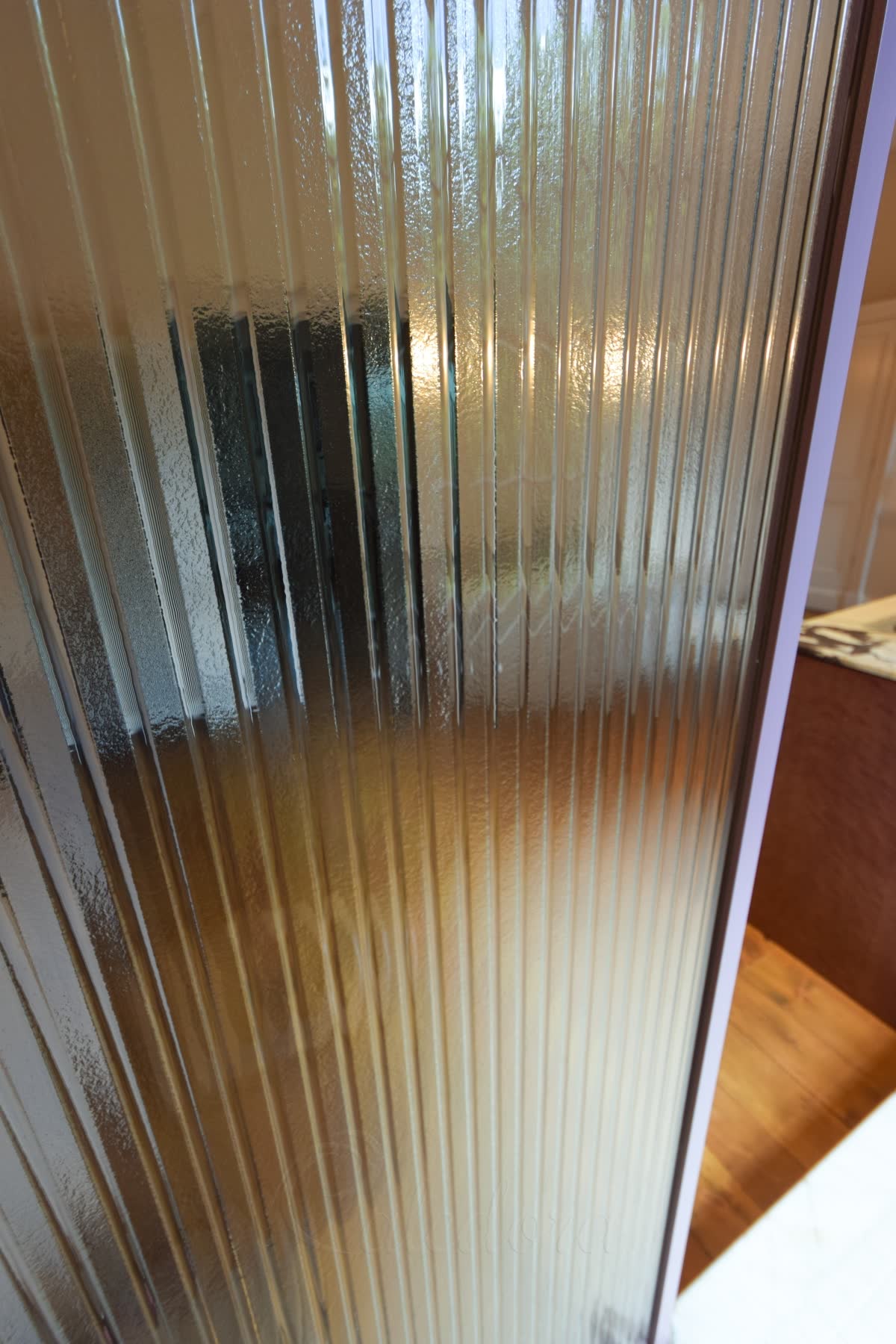 Close view of kiln-formed glass — wide rounded ribs melted into the sheet rather than rolled, the surface between them lightly textured, with the purple powder-coated frame edge visible at the side