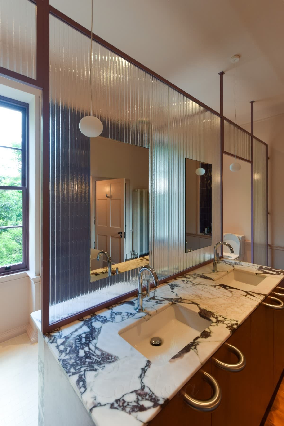 Kiln-formed glass screen with wide bespoke ribs in a purple powder-coated frame, dividing a bathroom above a marble double vanity