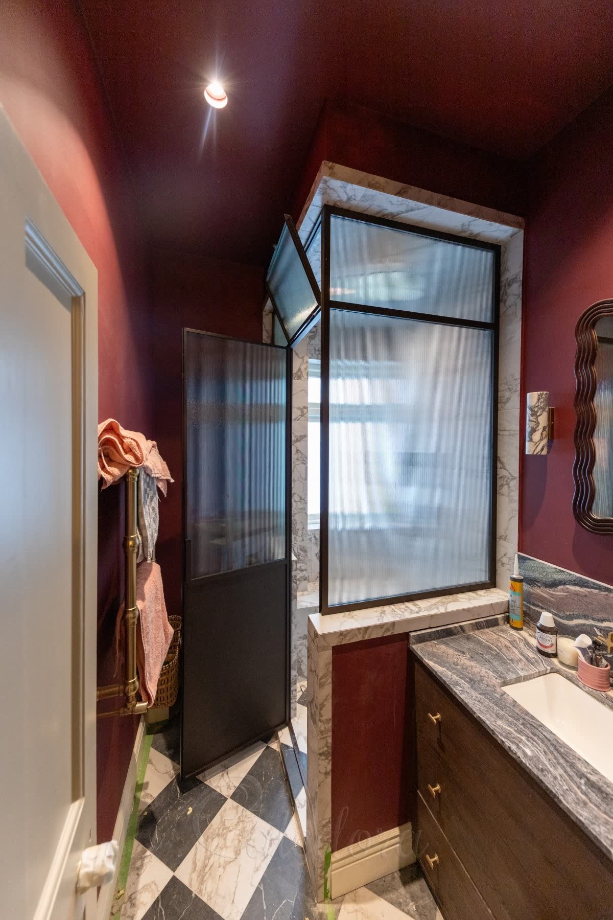 Reeded glass shower enclosure in a dark bronze frame in a burgundy bathroom with marble reveals and a chequerboard marble floor