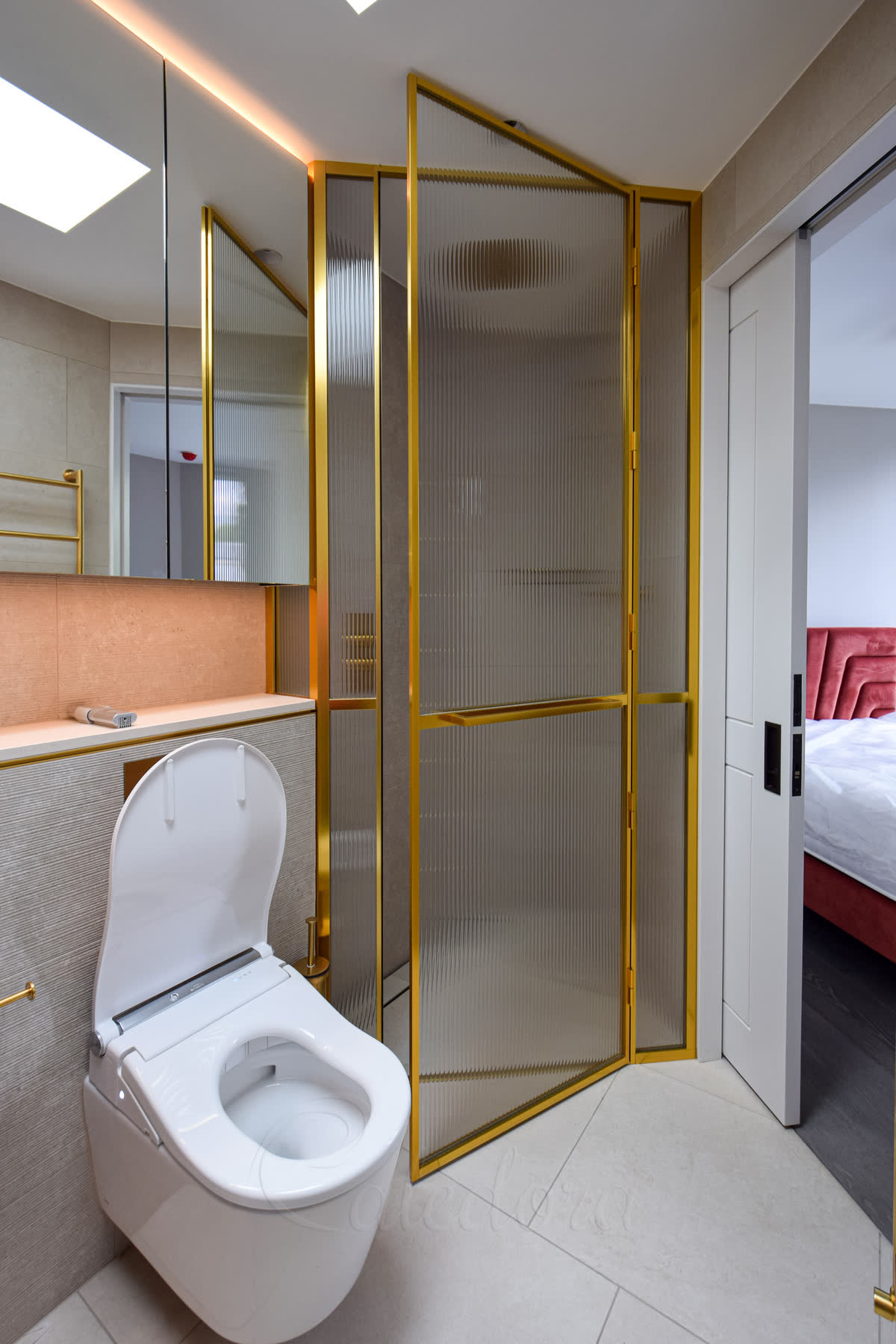 Reeded glass corner shower enclosure in a polished gold frame with a matching gold handle, in a bright bathroom