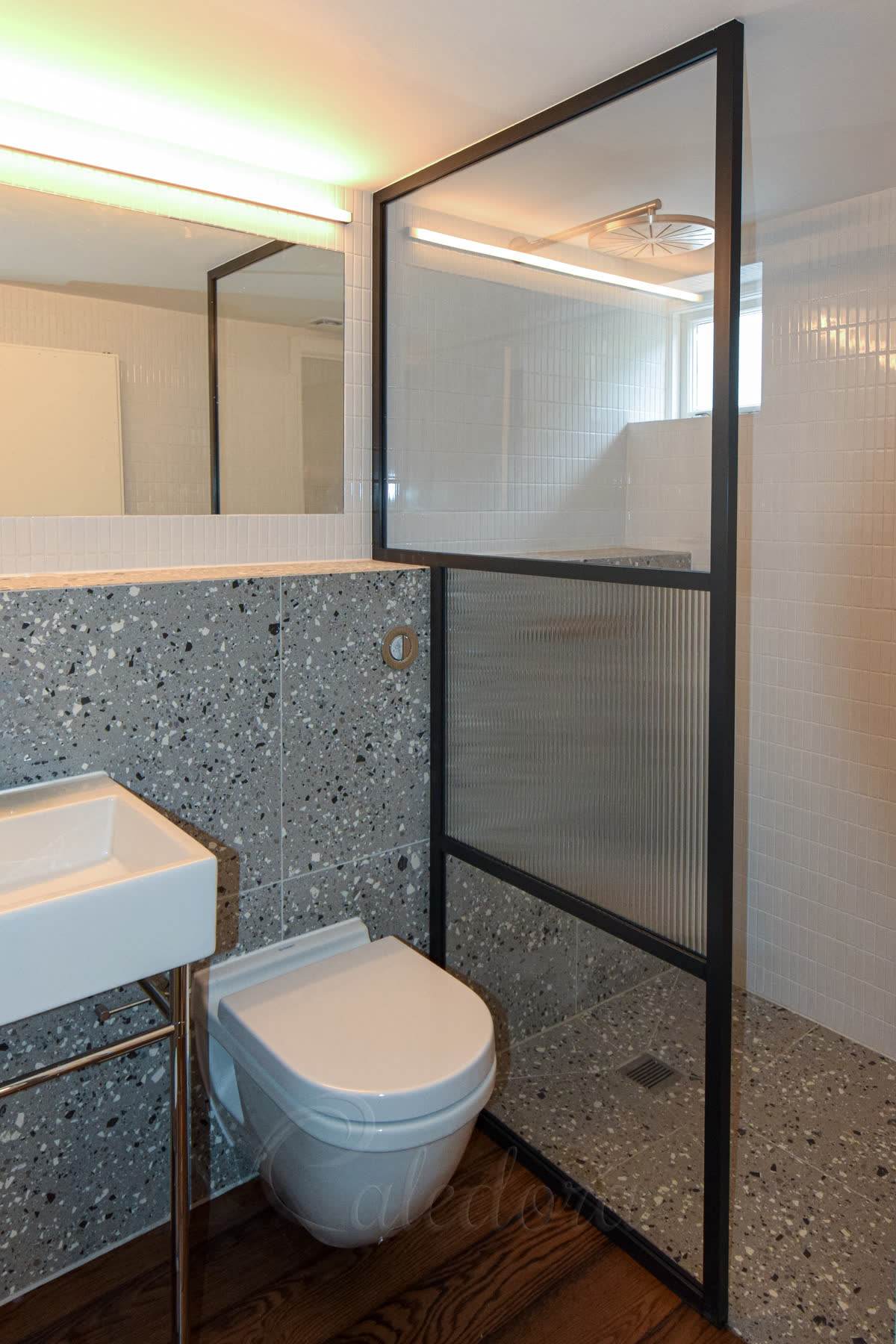 Reeded glass shower screen in a black grid frame fixed around a half-wall shelf