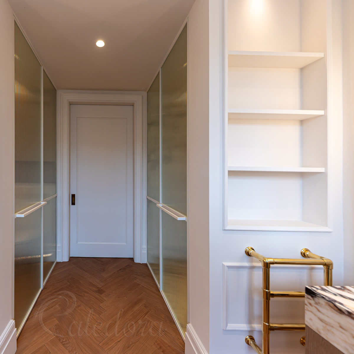 Reeded glass in white painted frames — a pair of doors set into a panelled corridor, the pale frames dissolving into the joinery beside brass towel rails and a herringbone oak floor