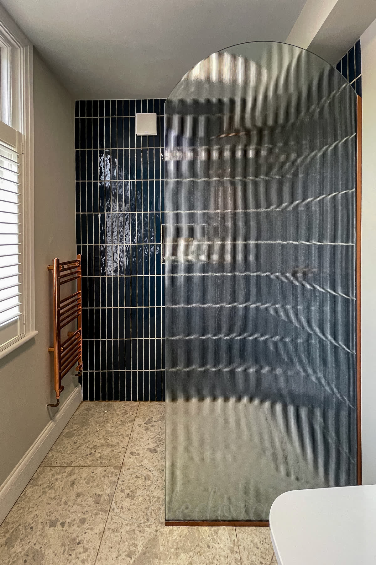 Arched custom shower screen with fluted glass and copper fixtures creating unique walk-in design with dark tile feature wall