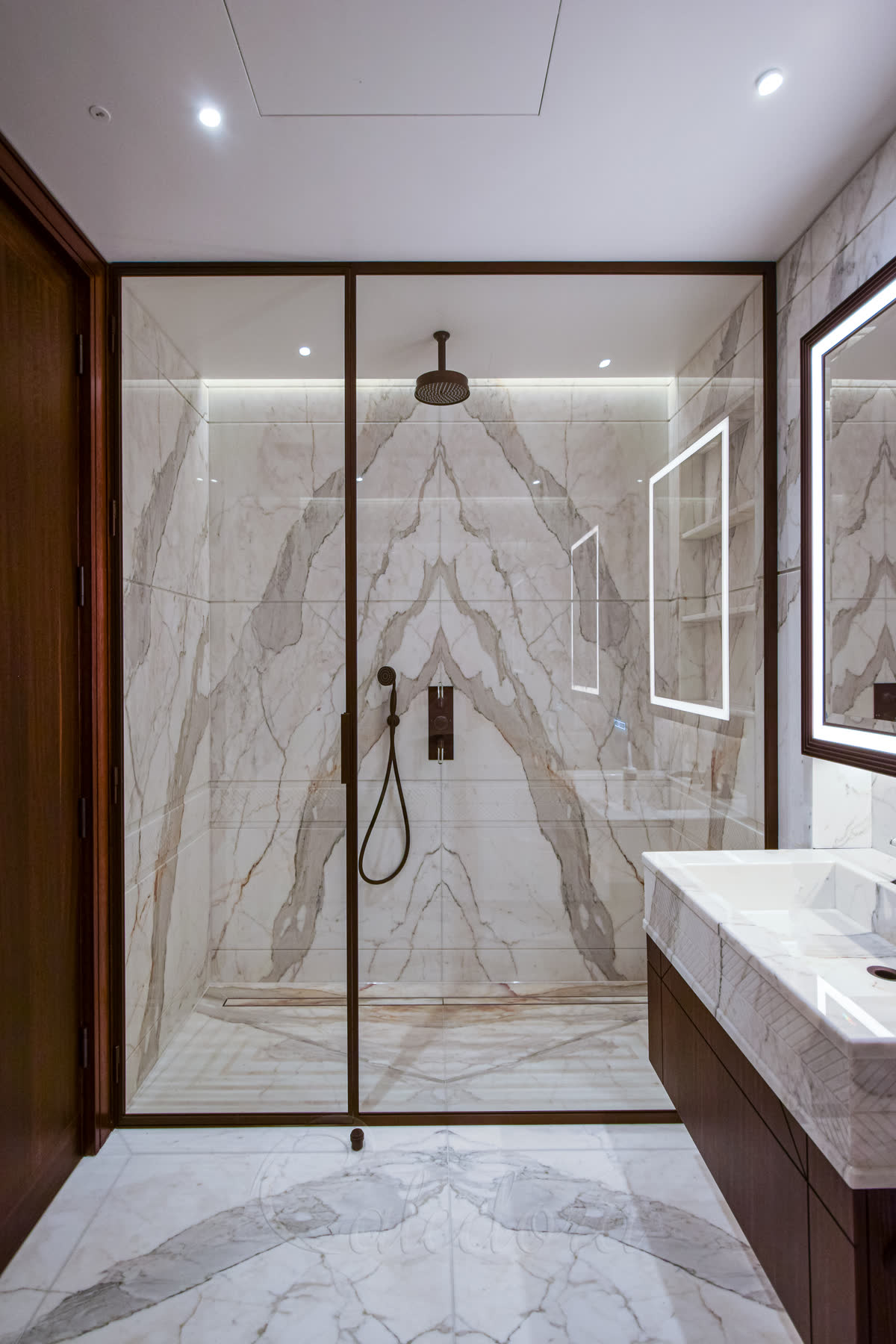 Bespoke shower enclosure with bronze frame, full-height large design and walk-in floor featuring book-matched marble walls in luxury bathroom