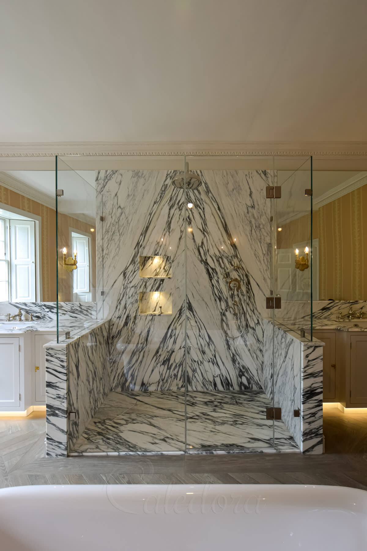 Bespoke shower enclosure mounted on book-matched arabescato marble half-walls with frameless glass panels above and a hinged door, in period bathroom