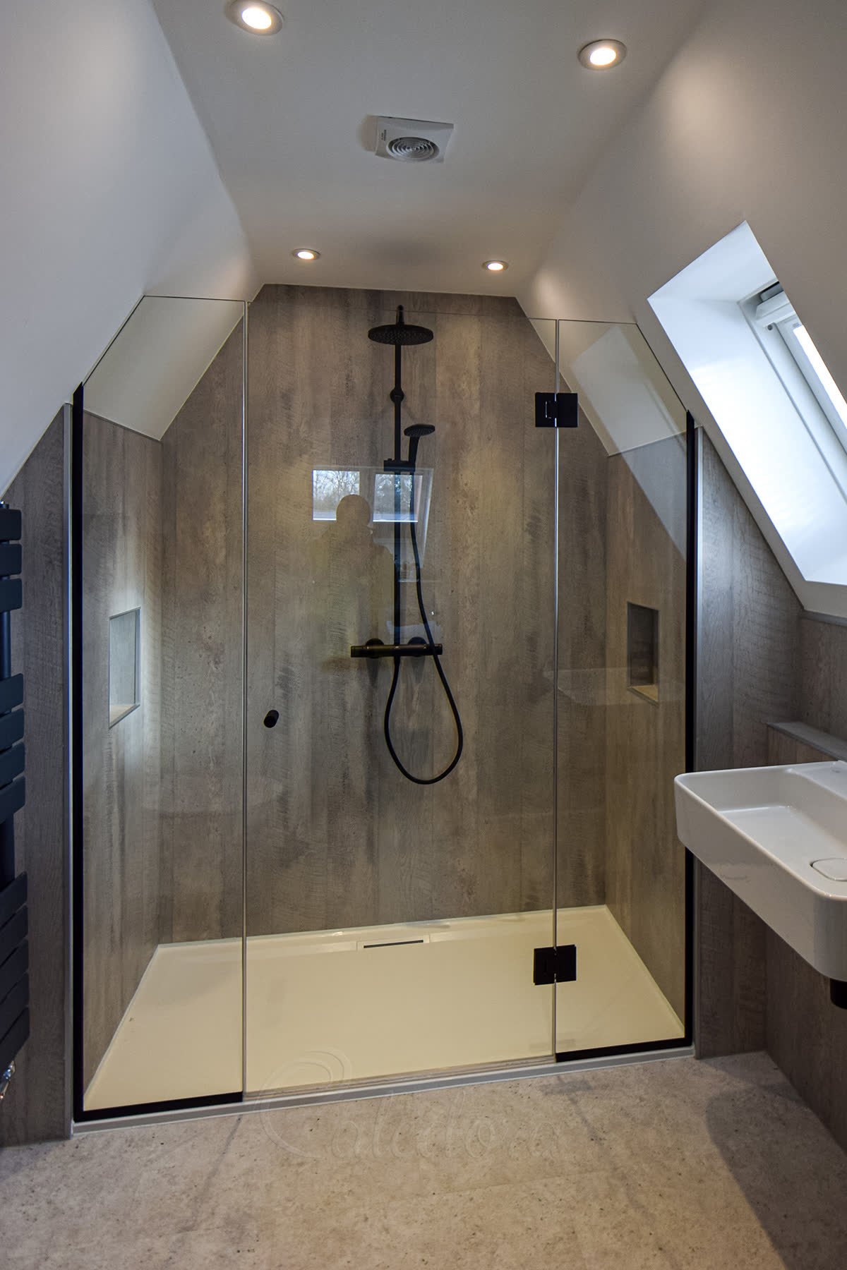 Frameless bespoke shower enclosure with two glass sides cut to follow loft eaves, brass fixtures and patterned floor in period green-tile bathroom