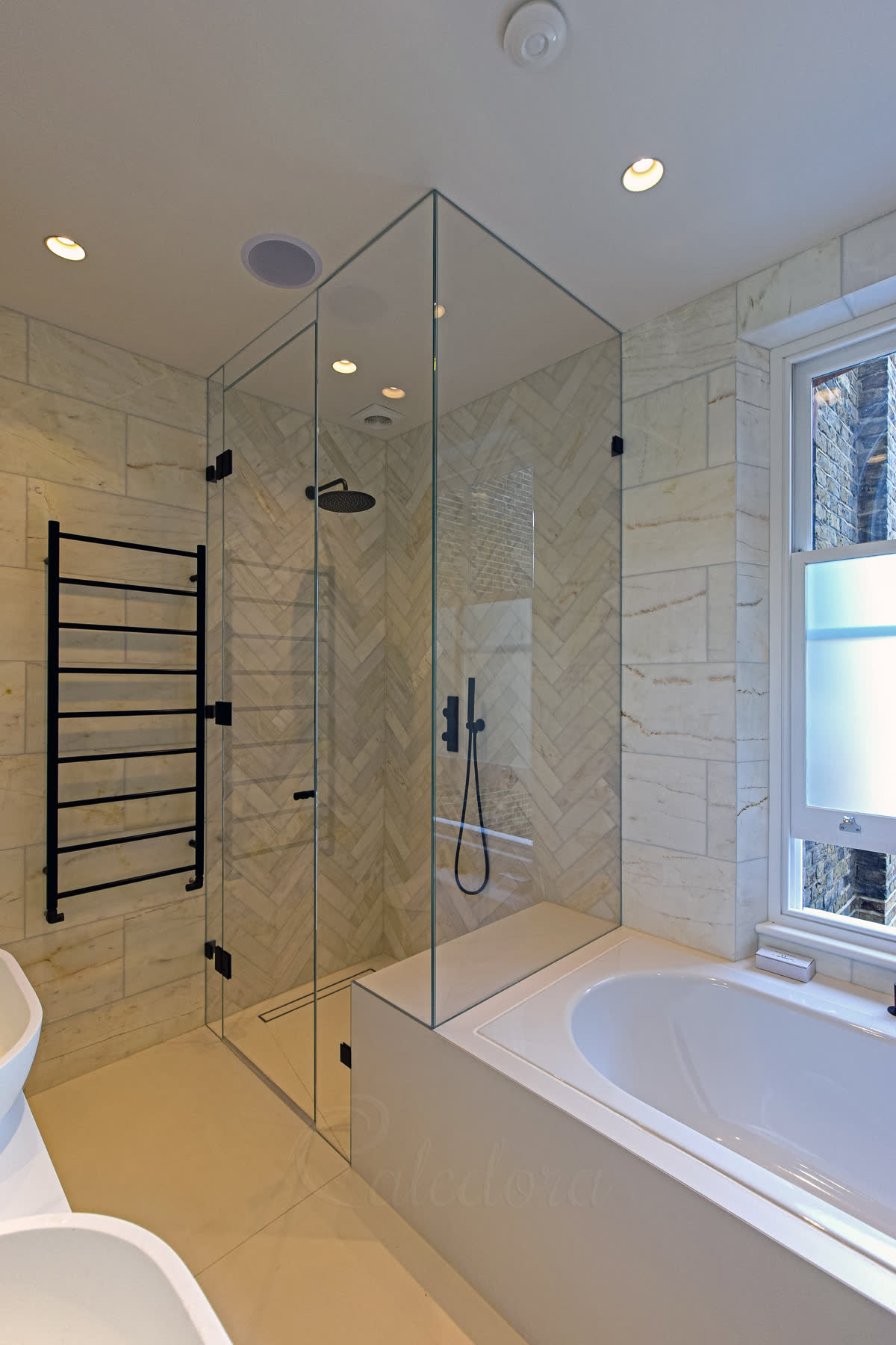 Frameless bespoke shower enclosure standing over the bath with herringbone marble interior, period sash window and dark hardware