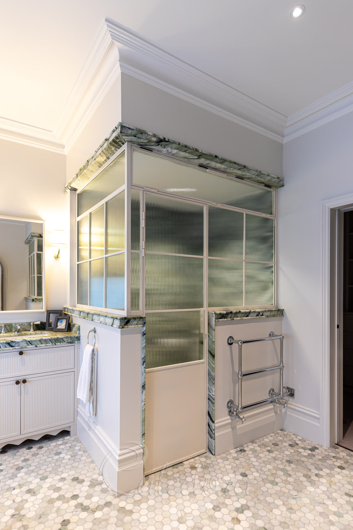 Bespoke shower enclosure with rare white grid frame, reeded glass panels and transom window above door built around marble-topped half-walls