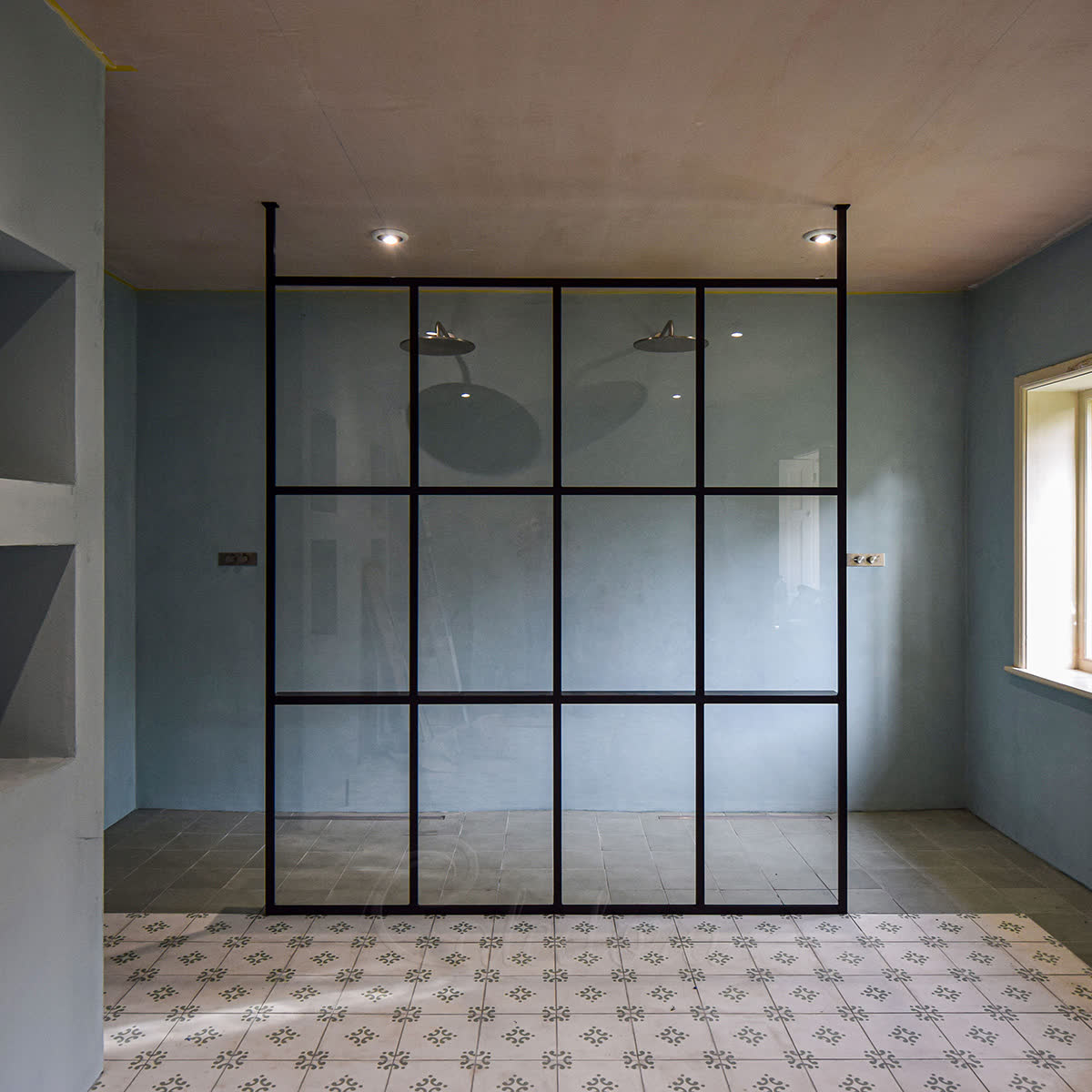 Bespoke walk-in shower screen with black-framed grid panel between two full-height structural posts, integrated shelf and double showerheads
