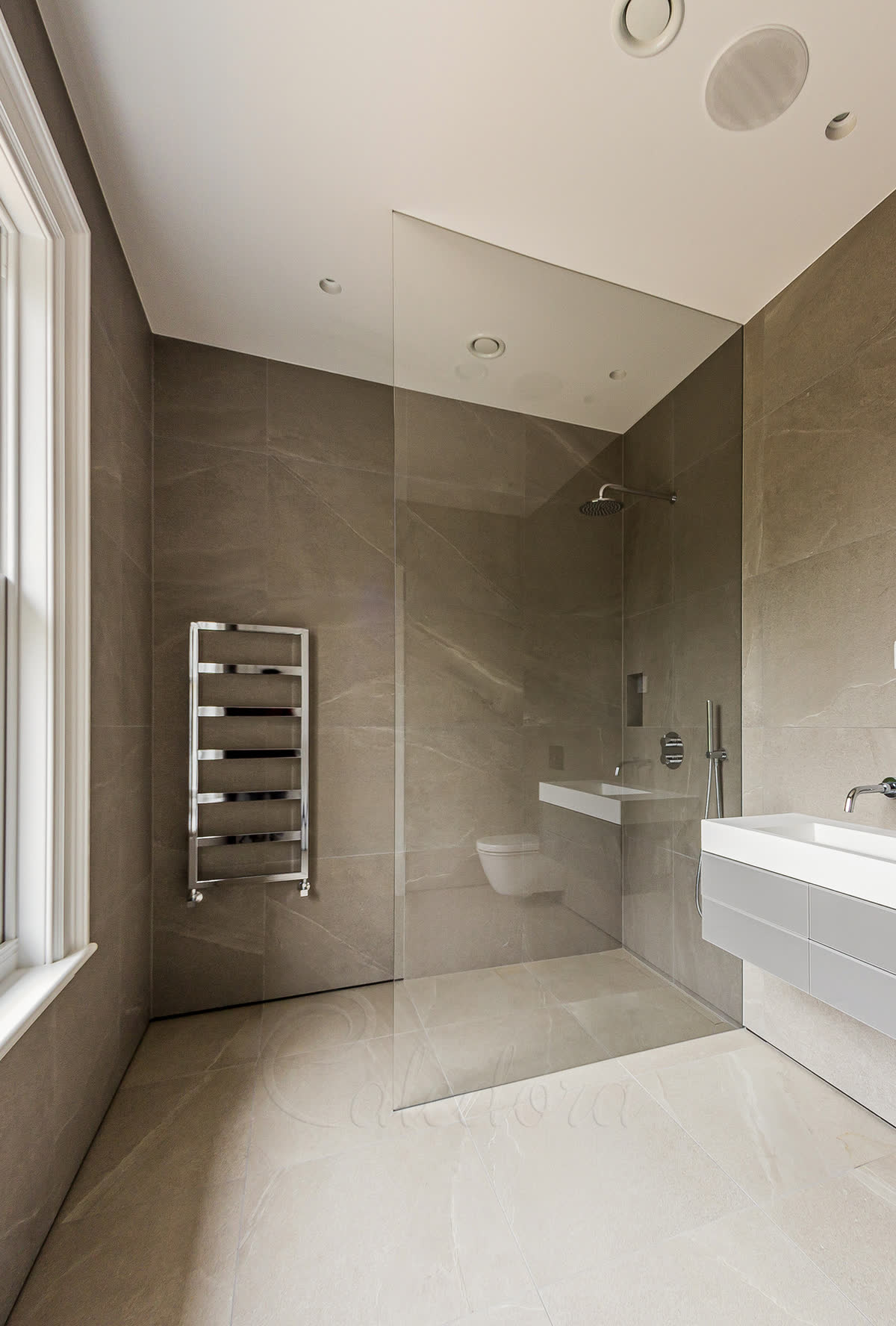 Bespoke frameless shower screen set into a wall recess with stone-grey large-format tiles and integrated bath area
