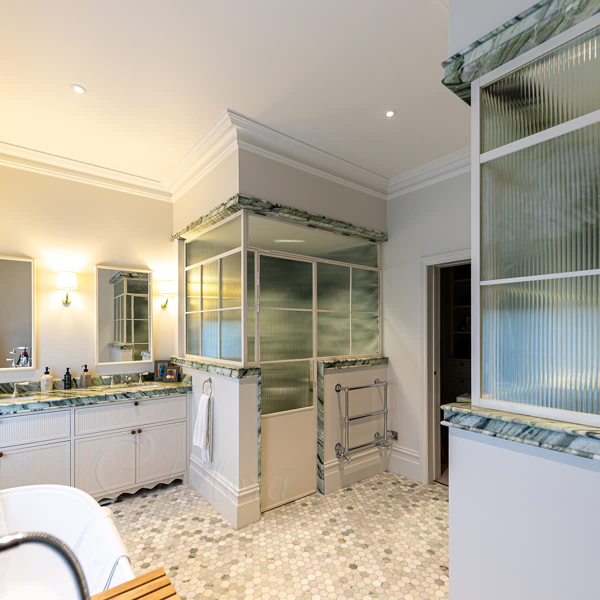 Framed bespoke shower enclosure with white powder-coated grid frame, transom window above the door, reeded glass panels and integrated half-wall in steam shower and WC layout