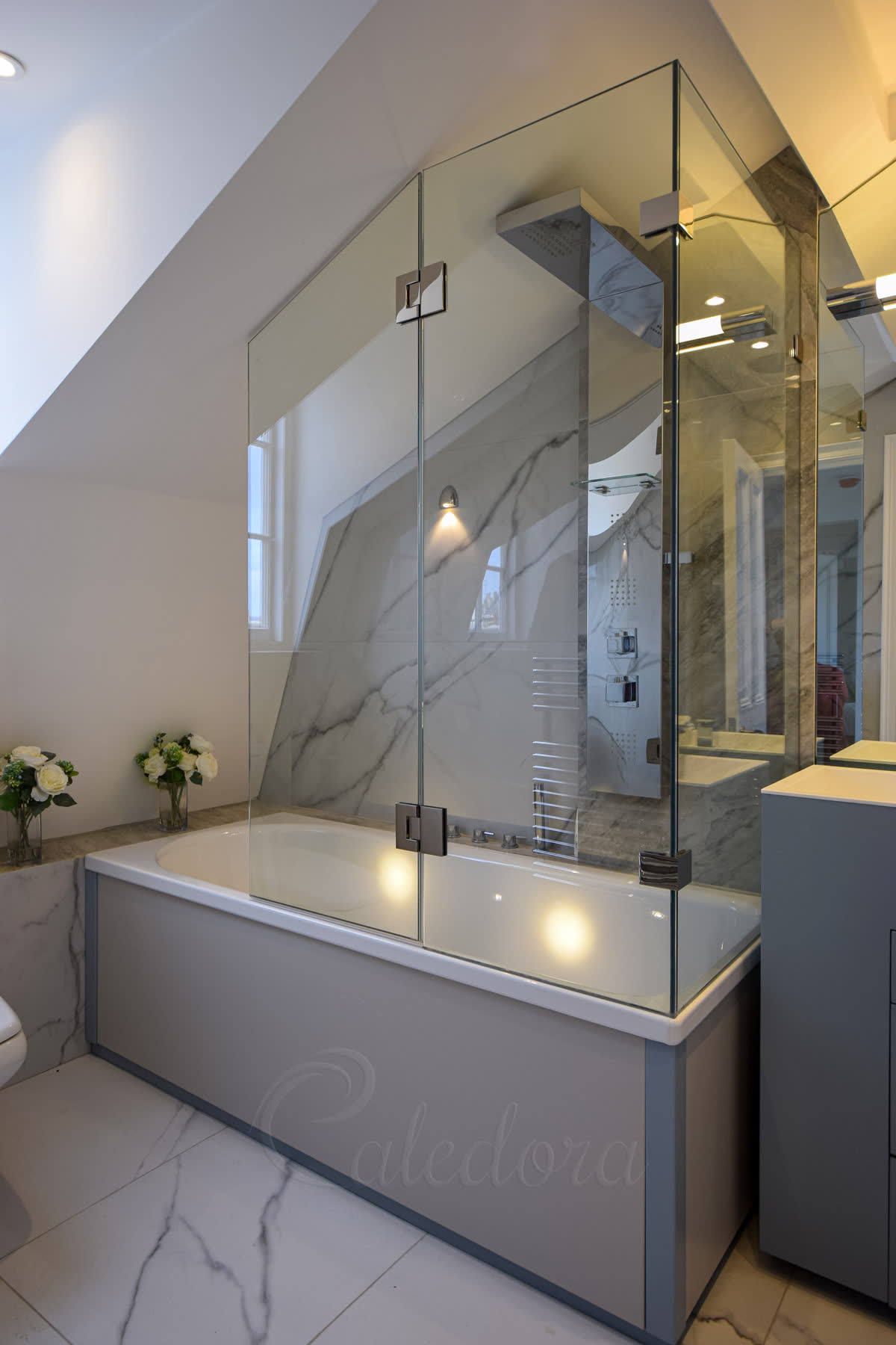 Loft bespoke shower screen shaped to follow sloped ceiling with nickel hinges over marble bath in converted space