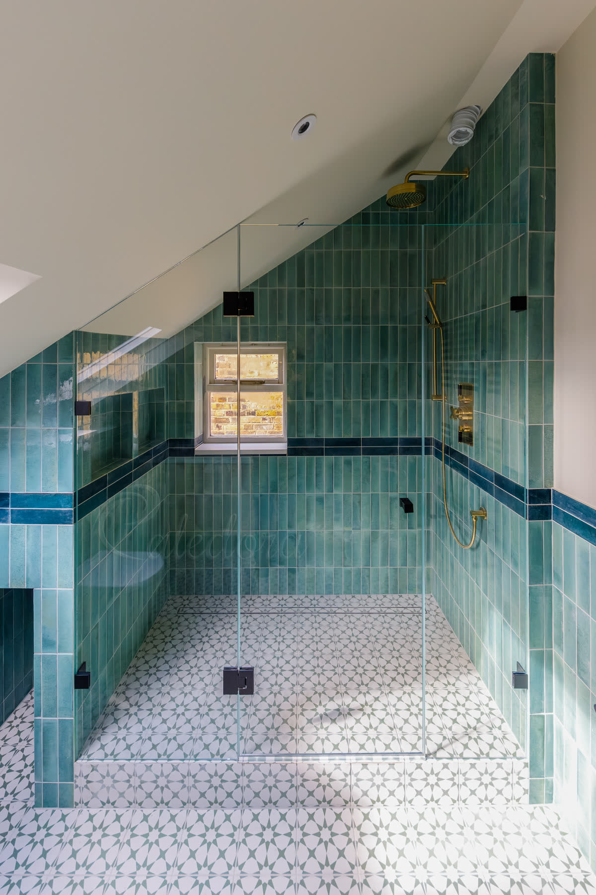 Loft frameless custom shower enclosure with one side shaped to follow sloped ceiling and black hinges in green tiled bathroom