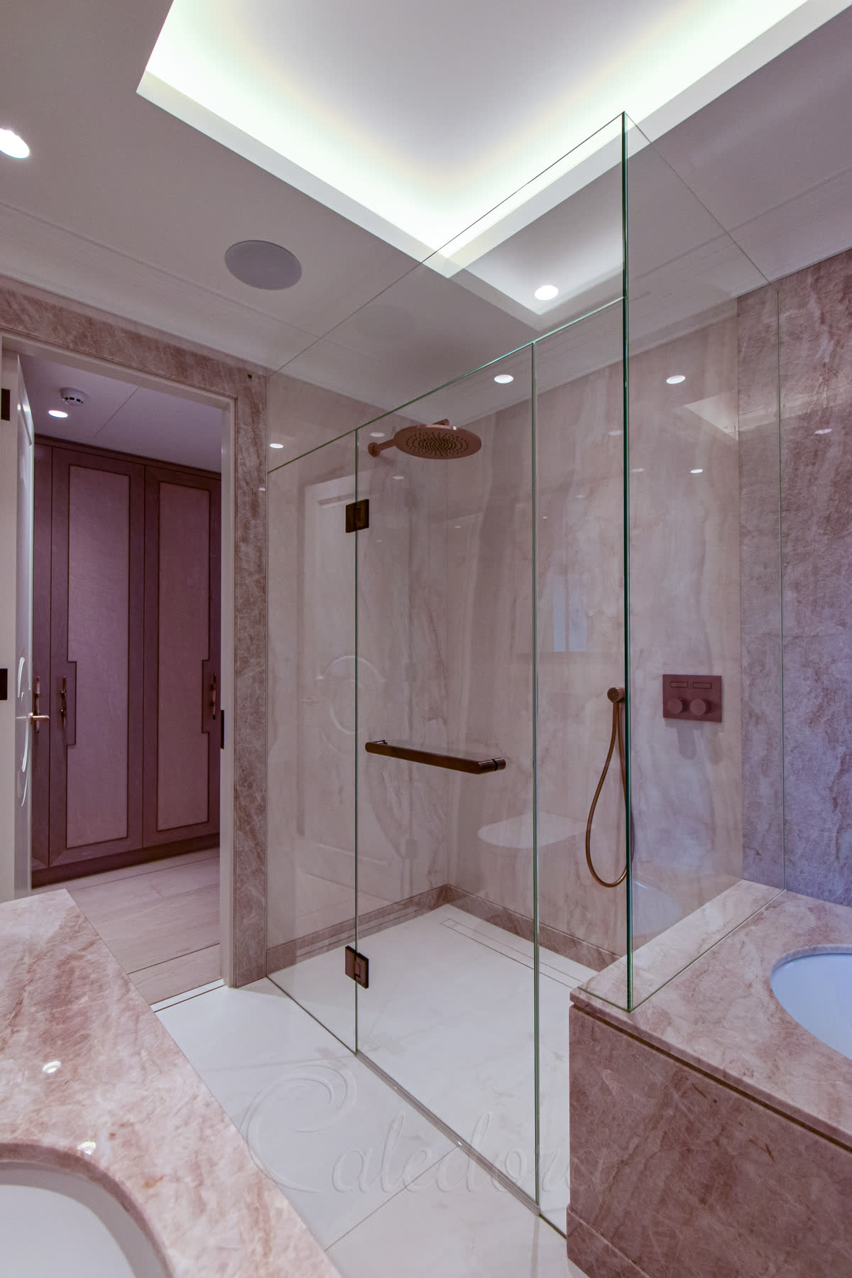Made to measure shower enclosure frameless with antique copper hinges and towel rail, partially over marble bath with recessed glass panels