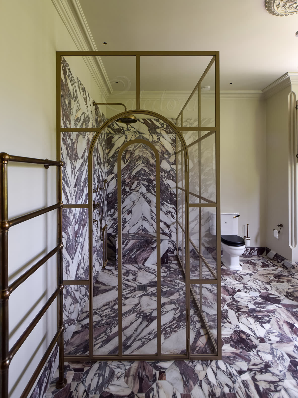 Corner glass shower enclosure with light-grey arched door and grid frame, opening into a book-matched purple-veined marble interior in a luxury London bathroom