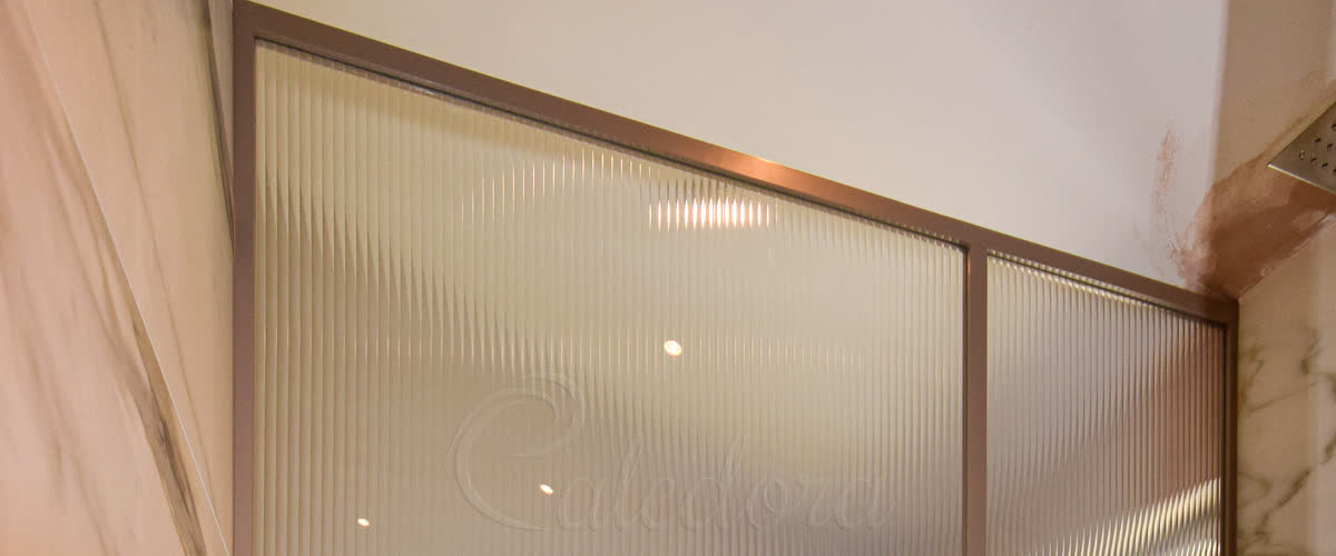 Cropped detail of a bronze-frame shower glass screen with grid-style middle bar and fluted vertical-ribbed glass in a marble bathroom