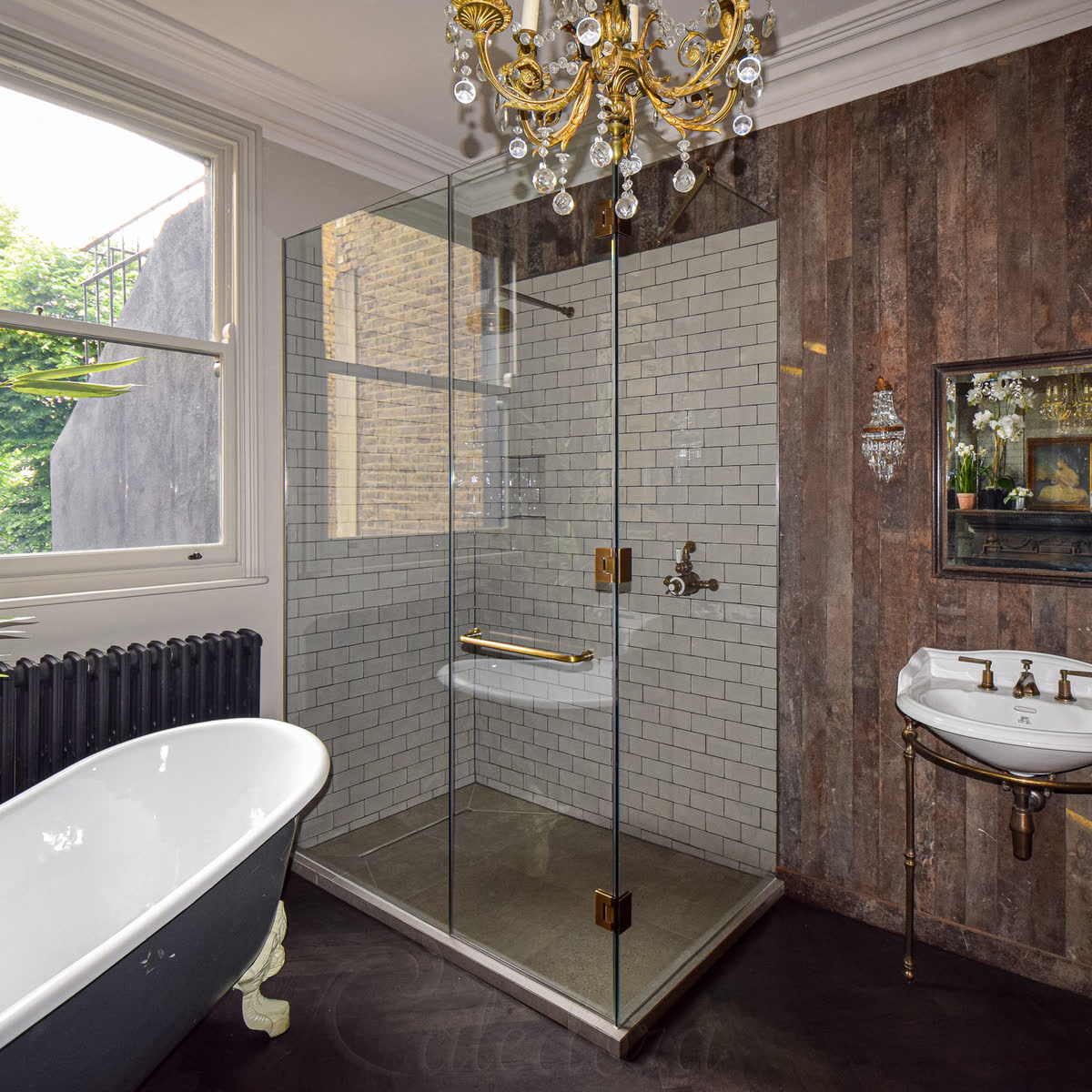 Frameless corner glass shower enclosure with brushed brass hinges and wall-recessed panels in a period bathroom