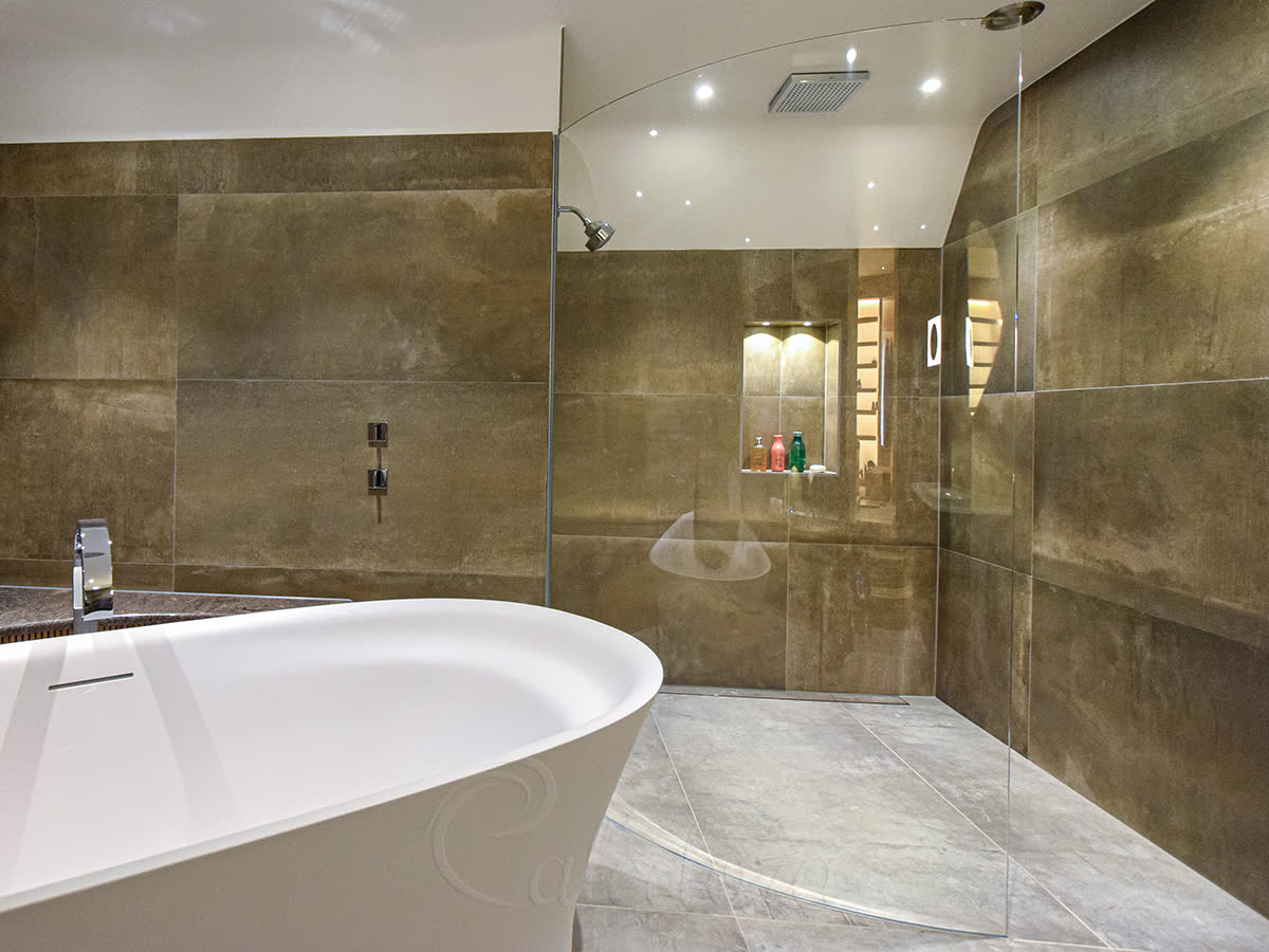 Frameless curved glass shower screen with wall-recessed installation and 8mm Ultra Clear toughened glass next to a freestanding bathtub in a luxury Sussex bathroom