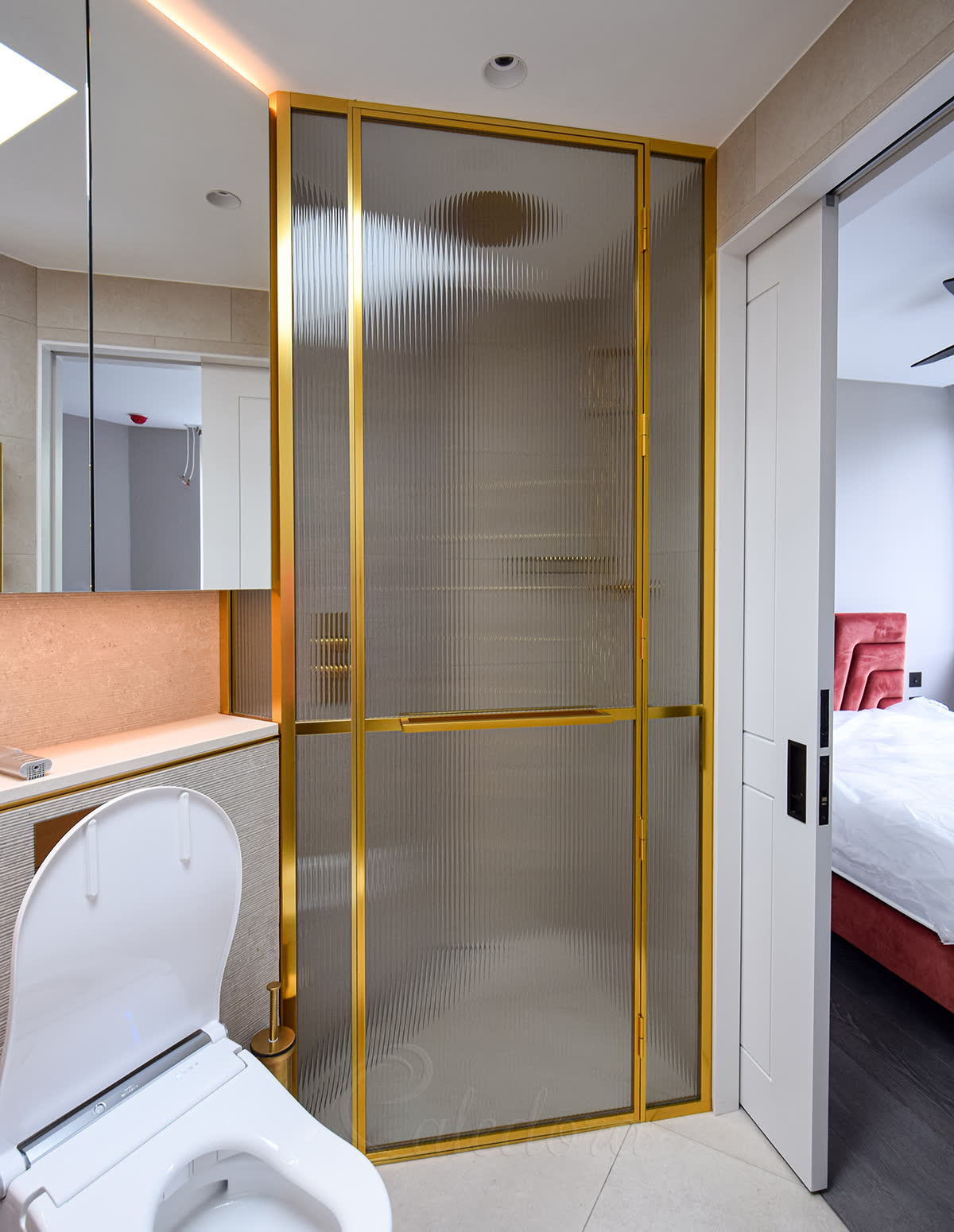 Polished gold framed inline glass shower enclosure with reeded laminated glass, 135-degree angled layout and integrated horizontal towel rail in a London bathroom