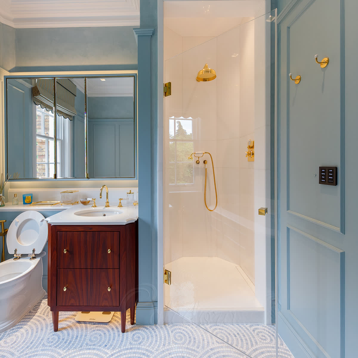 Hinged shower glass door with polished brass hardware in a blue-panelled period bathroom with brass shower fixtures