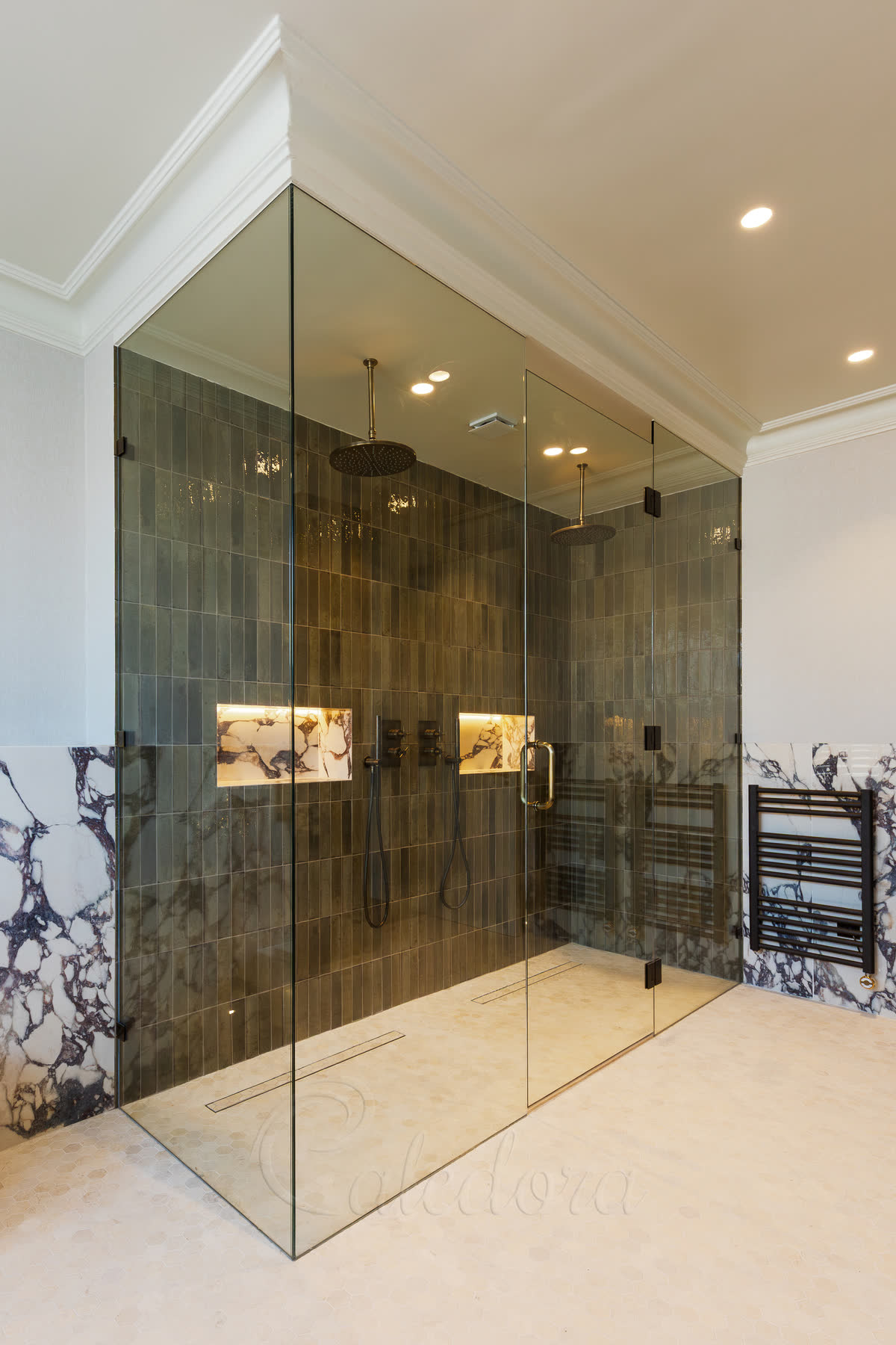 Large frameless corner glass shower enclosure with antique brass hardware, double ceiling-mounted showerheads, backlit LED niches and dark green tile walls in a period London bathroom