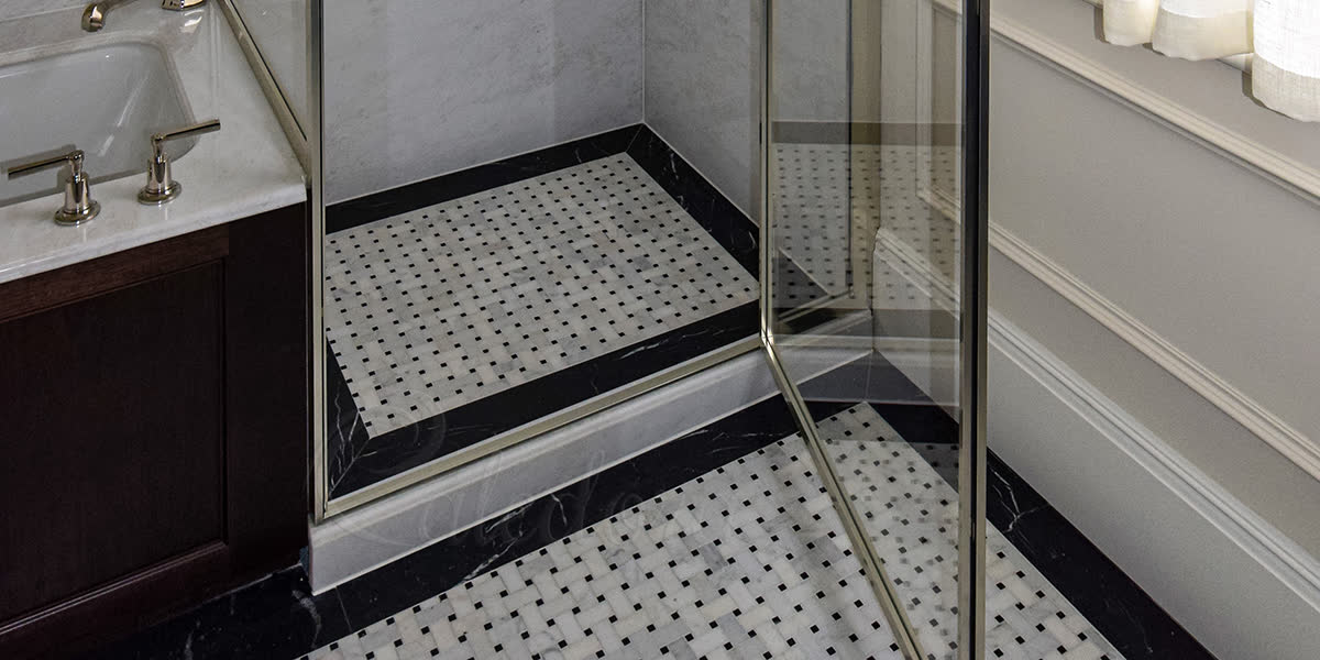 Cropped detail of a marble shower tray with raised plinth and basket-weave marble floor pattern