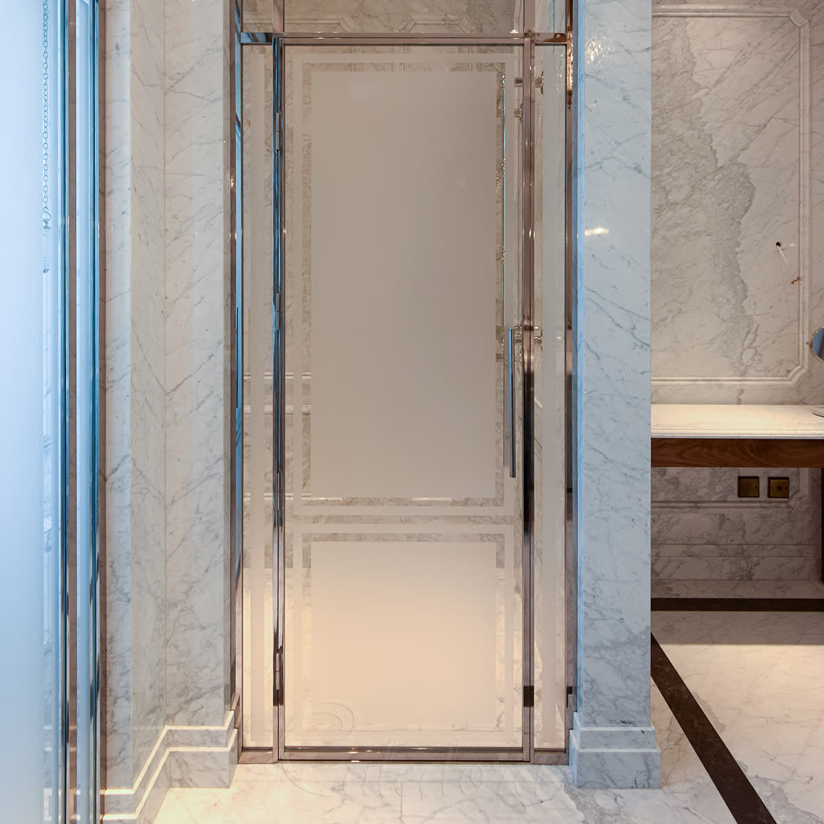 Mirror-polished nickel framed shower door with partially-sandblasted Ultra Clear glass, alcove-mounted between book-matched marble walls in a luxury London bathroom with crystal chandelier