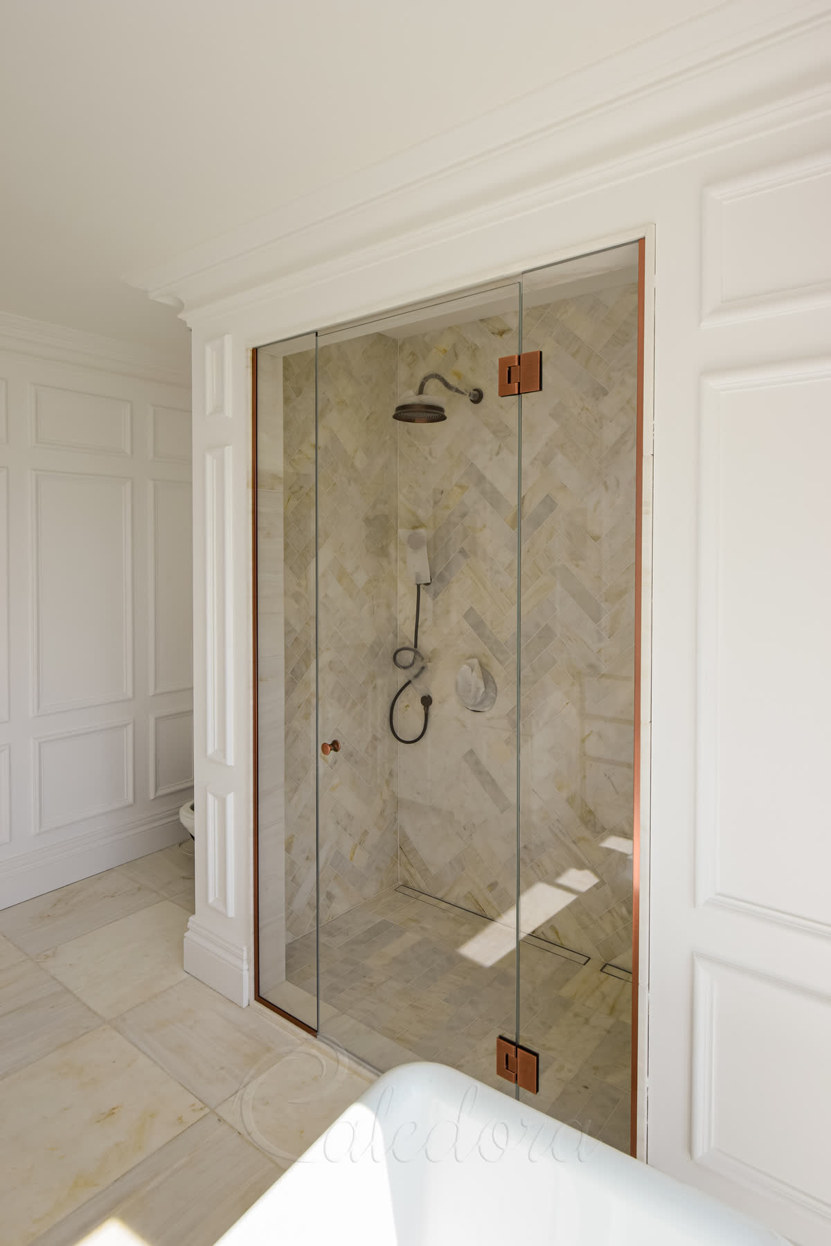 Side view of shower enclosure in a recess from the right showing a freestanding bath adjacent to ultra clear glass with antique copper hinges