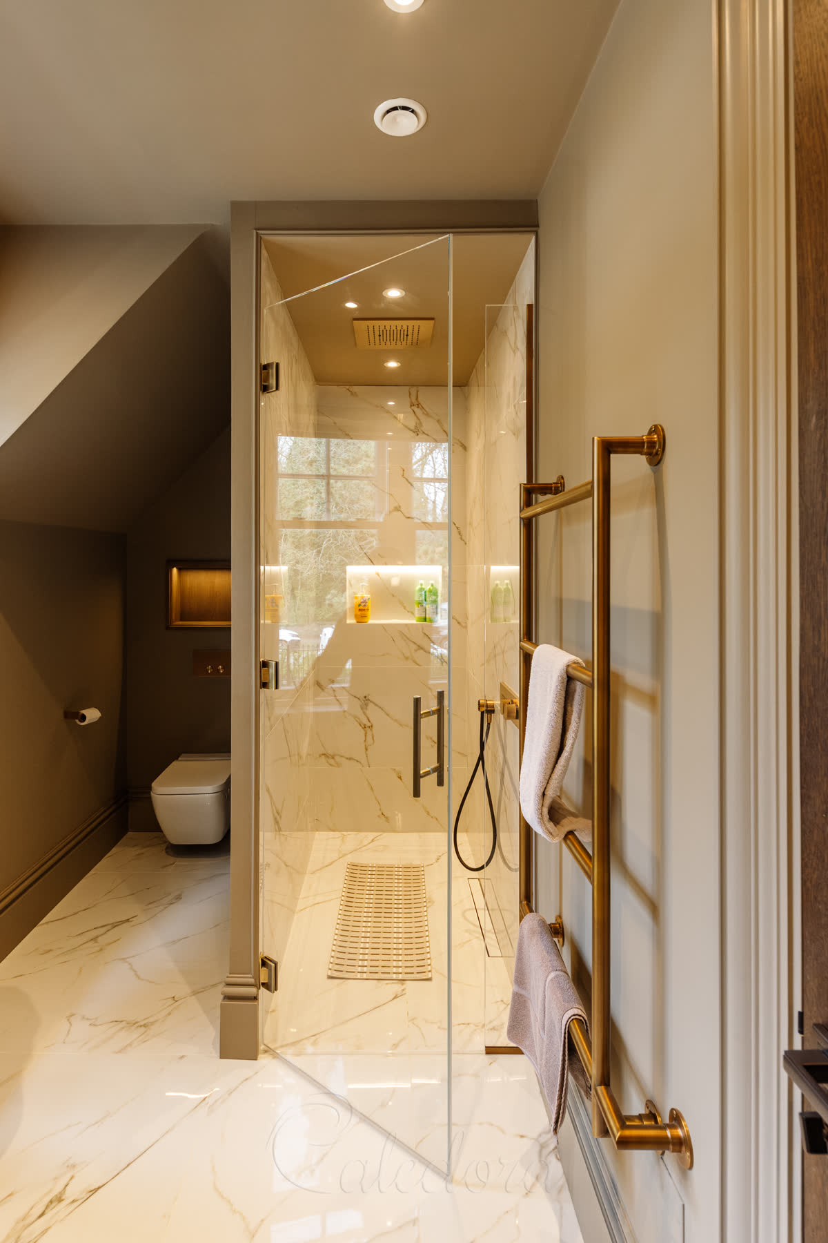 Antique brass shower door partially open with the minimalist bubble seal visible on the door perimeter and an acrylic threshold across the wet-room floor