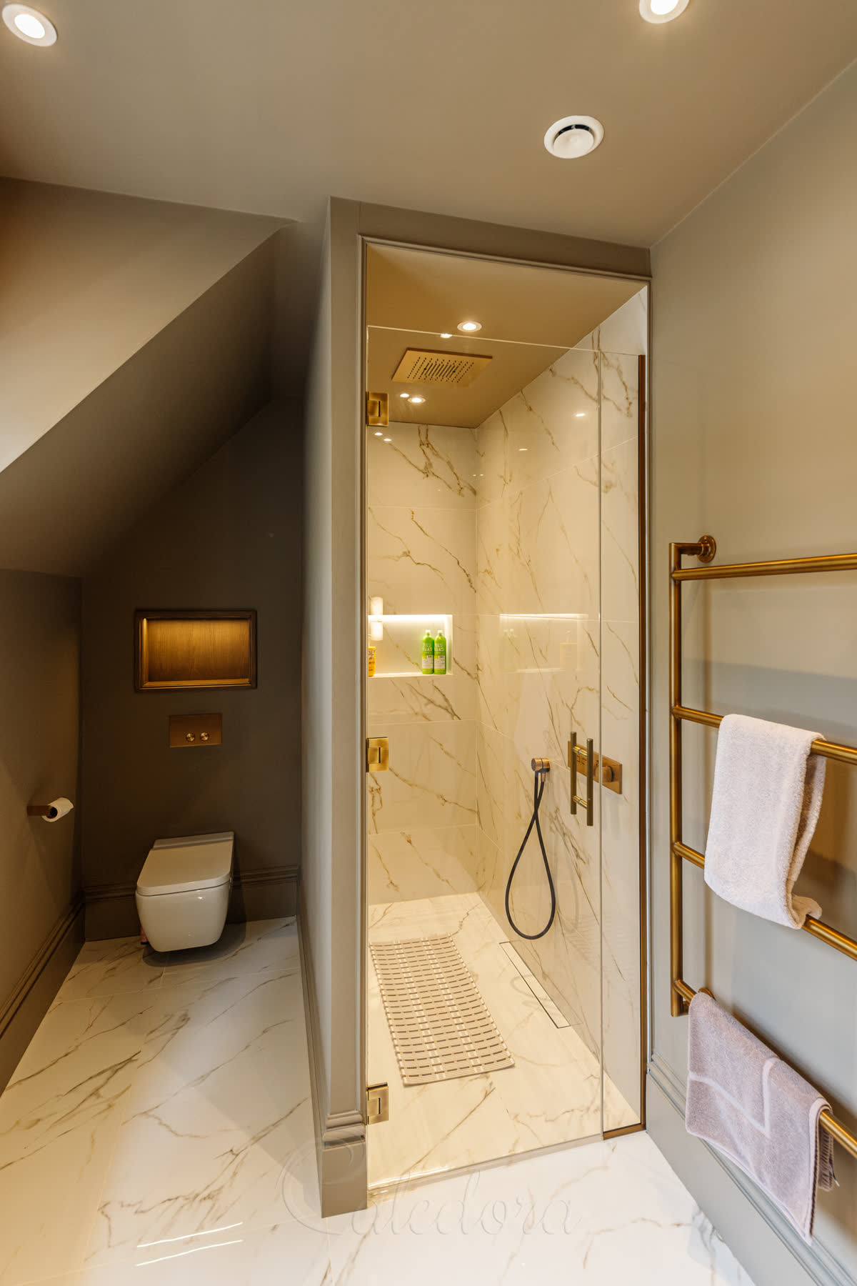 Angled view of the antique brass shower enclosure showing the slim inline fixed panel and a wall-mounted antique brass towel rail beside the glass