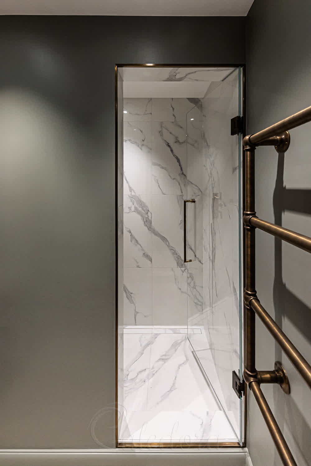 Antique brass shower door with client-supplied rail handle and ultra clear glass in marble bathroom