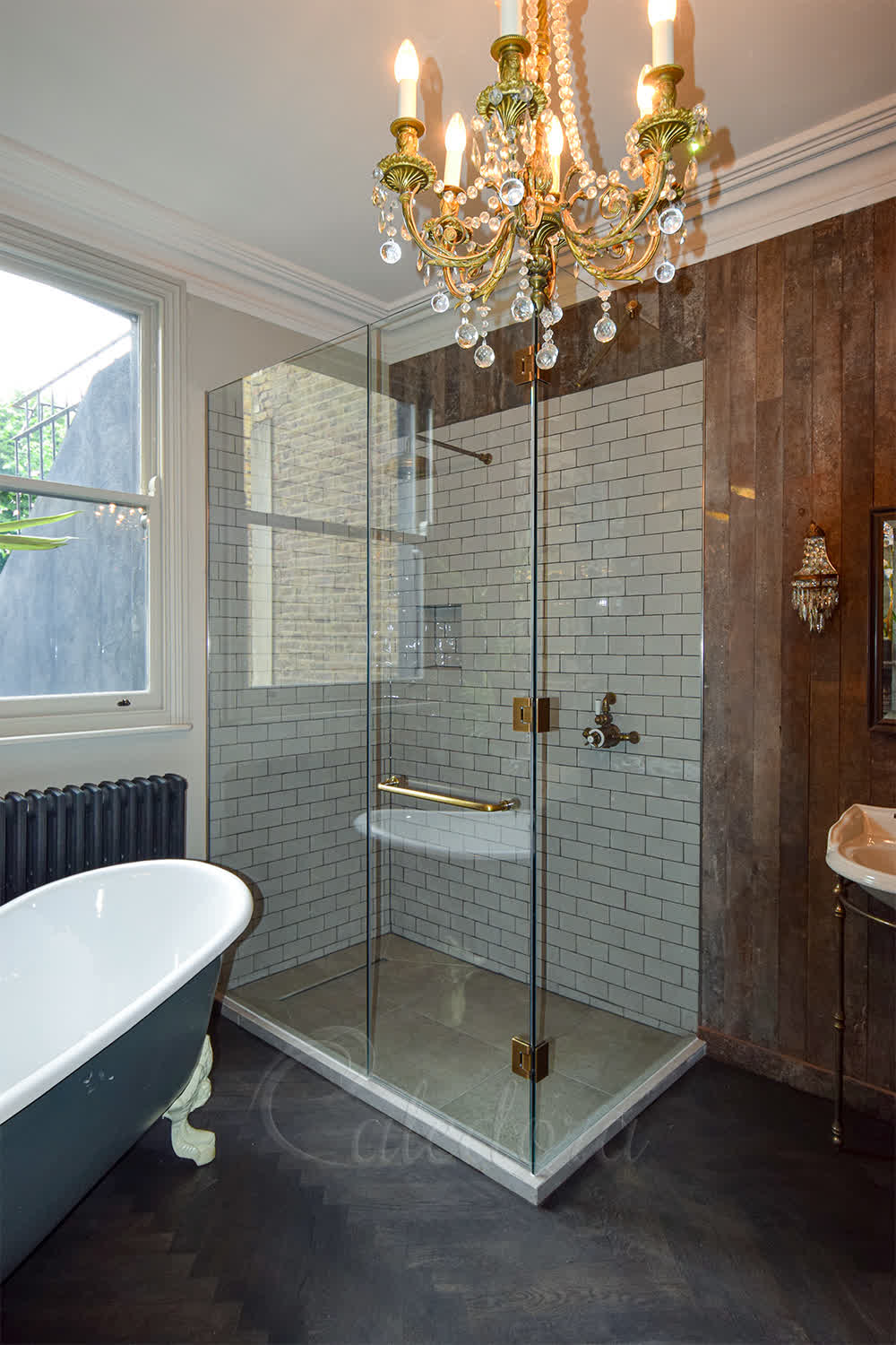Complete corner shower enclosure with antique brass hinges and tiled upstand in bathroom with ornate chandelier