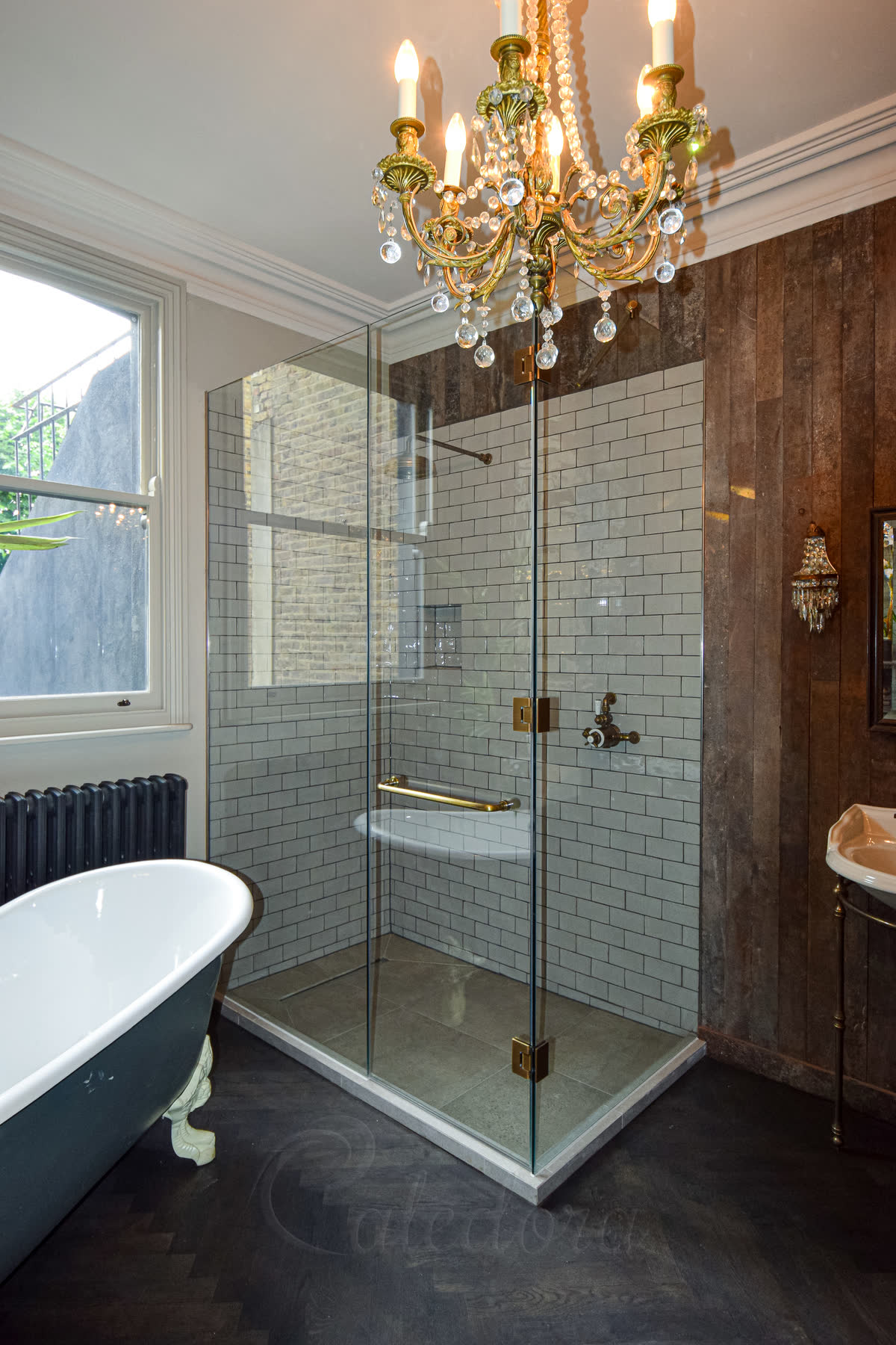 Complete corner shower enclosure with antique brass hinges and tiled upstand in bathroom with ornate chandelier