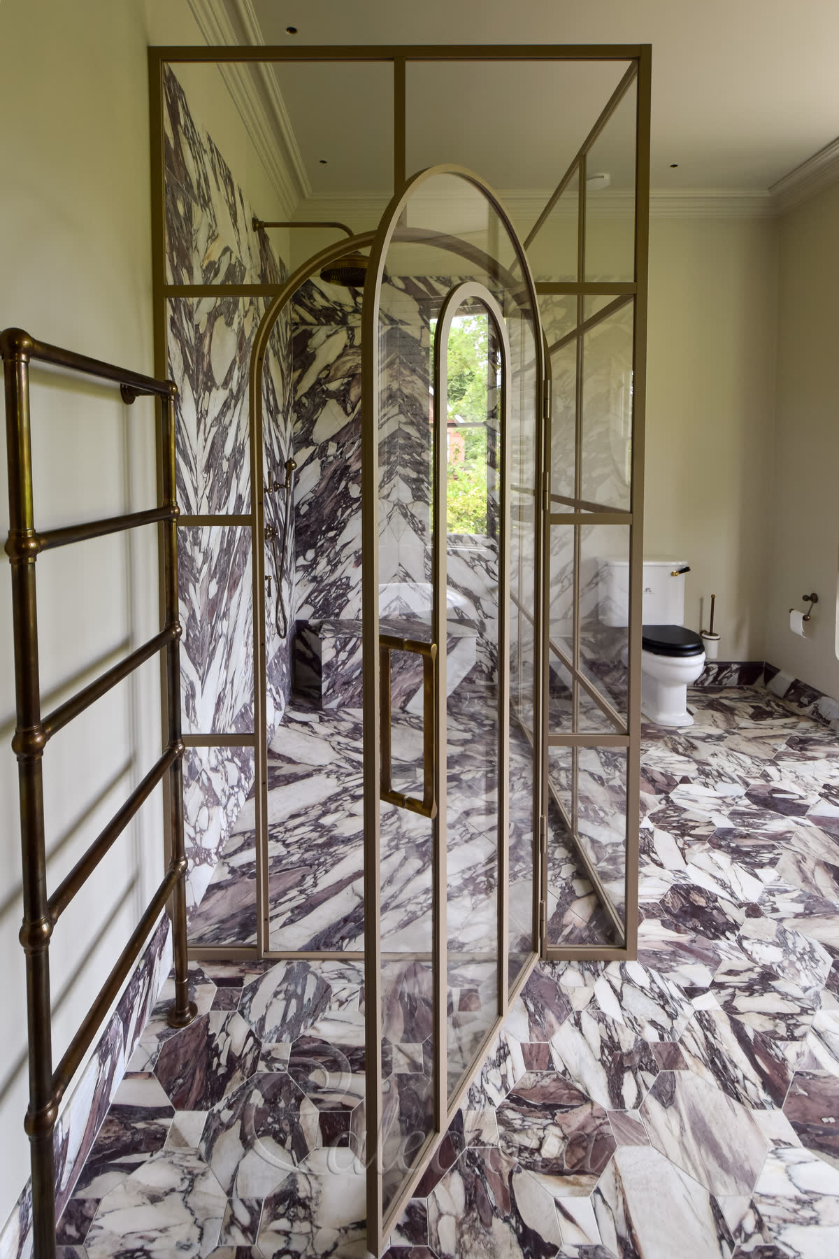 Corner view of arched shower enclosure with beige frame and marble surfaces