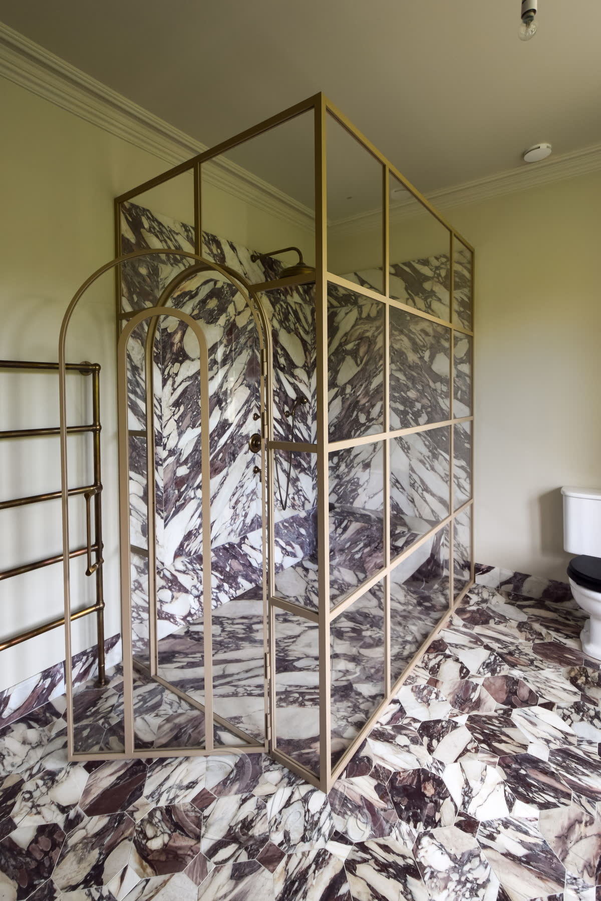 Wide angle view of arched shower door enclosure with beige towel rack