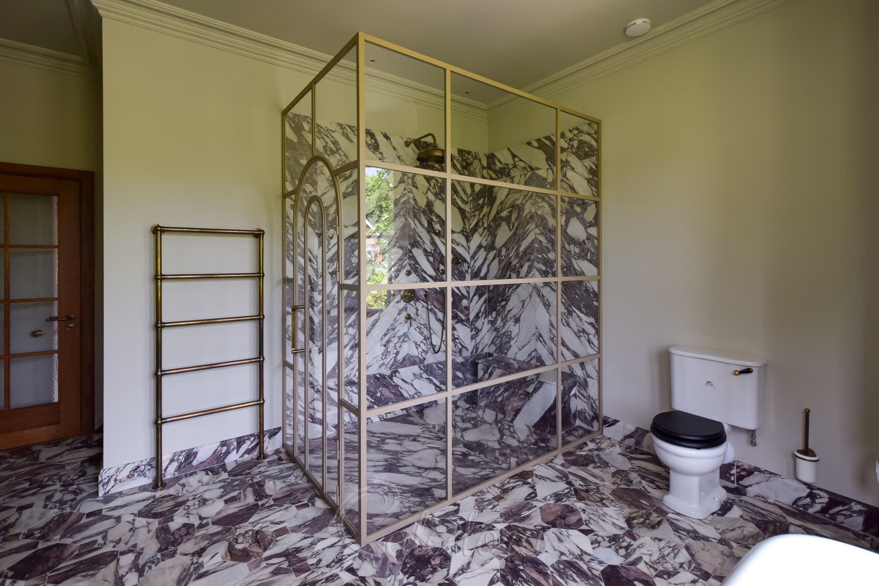 Full view of arched shower enclosure showing door and marble tiled walls