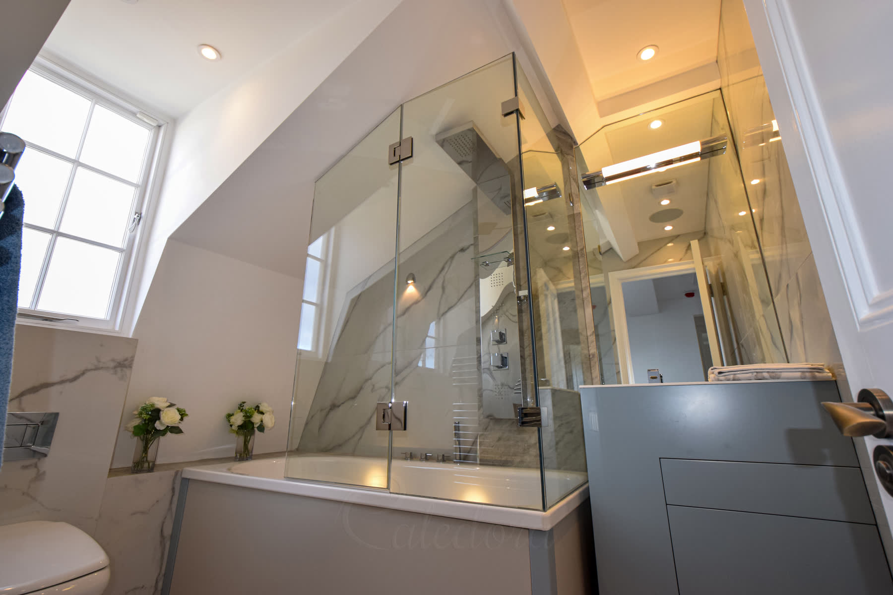 Complete bath shower enclosure installation under eaves with frameless glass panels and hinged access door