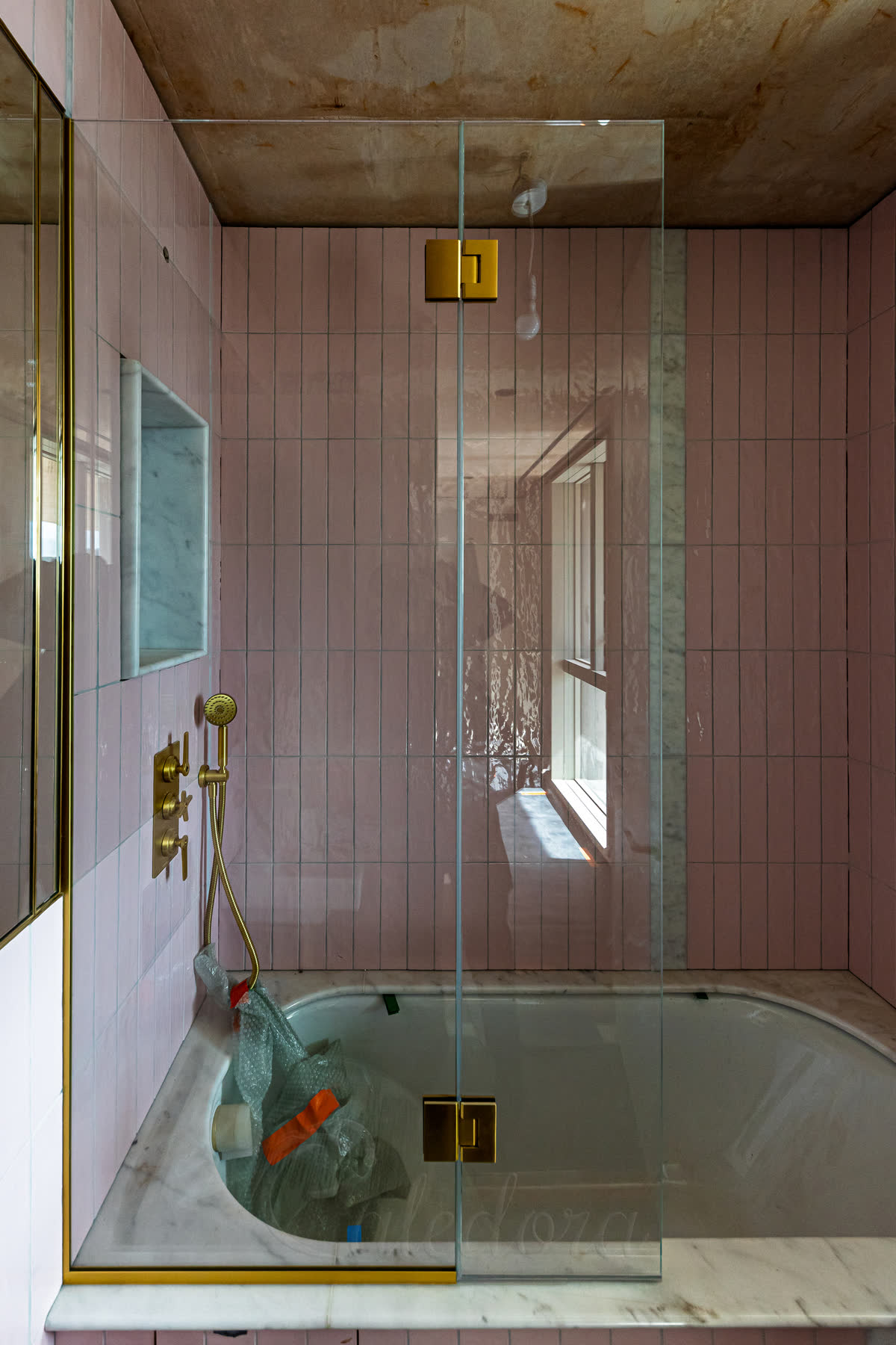 Bath shower screen with flipper panel in pink tiled bathroom with brushed brass hardware