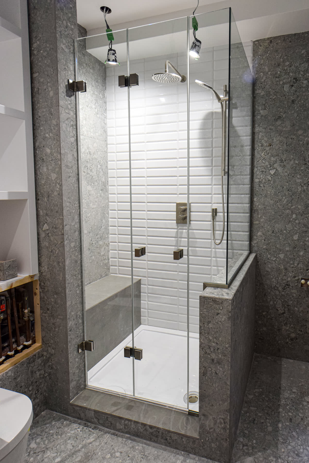 Brushed nickel bi-fold shower enclosure with closed folding door and glass cut-out around taps