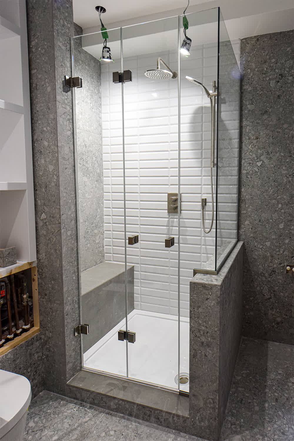 Brushed nickel bi-fold shower enclosure with closed folding door and glass cut-out around taps