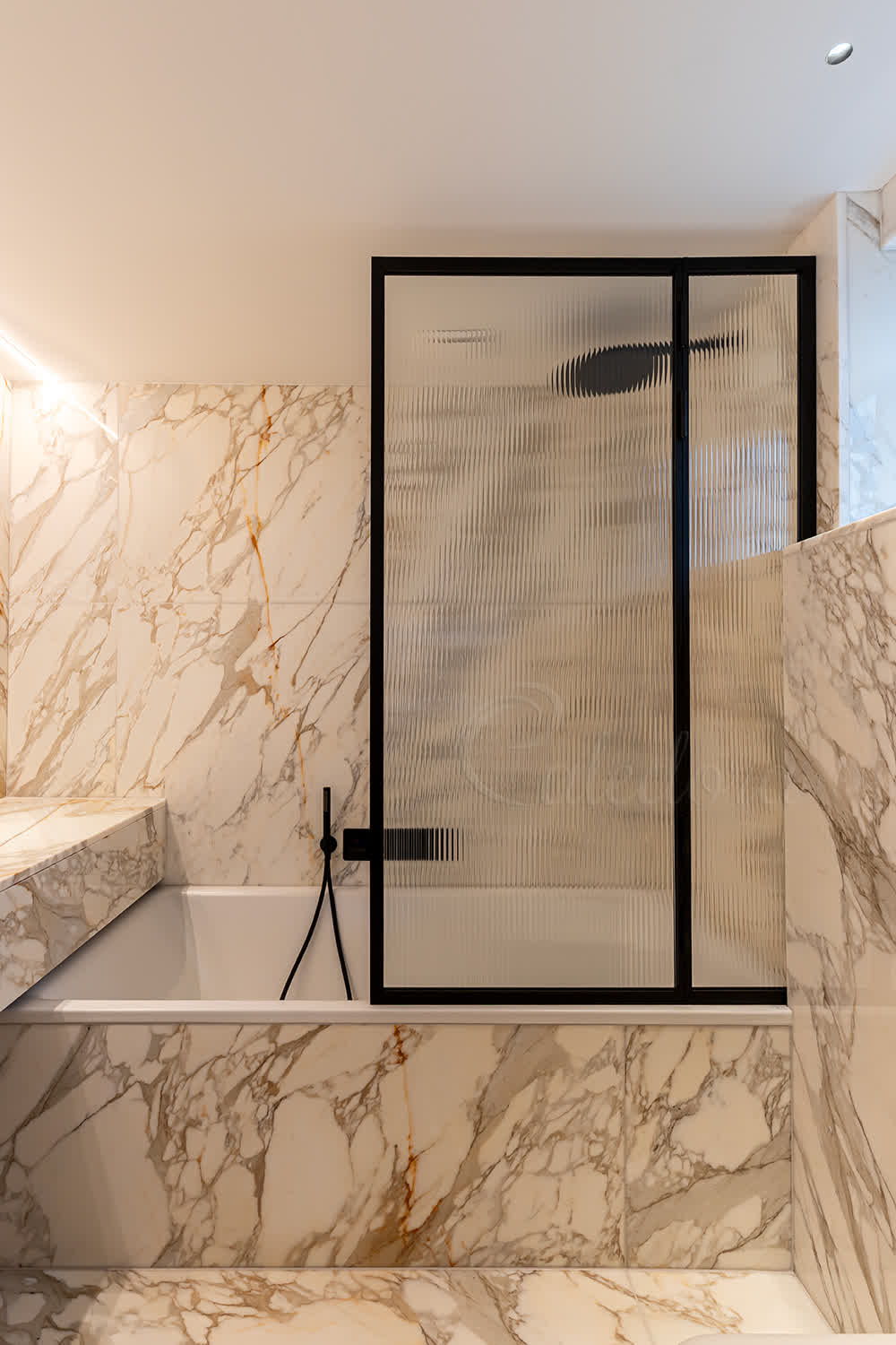 Elegant black framed folding bath screen with reeded glass in a luxury marble bathroom